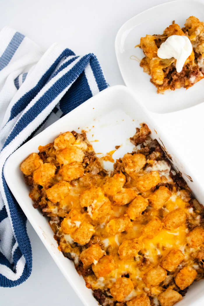 ground beef tater tot casserole in dish with serving on white plate nearby.