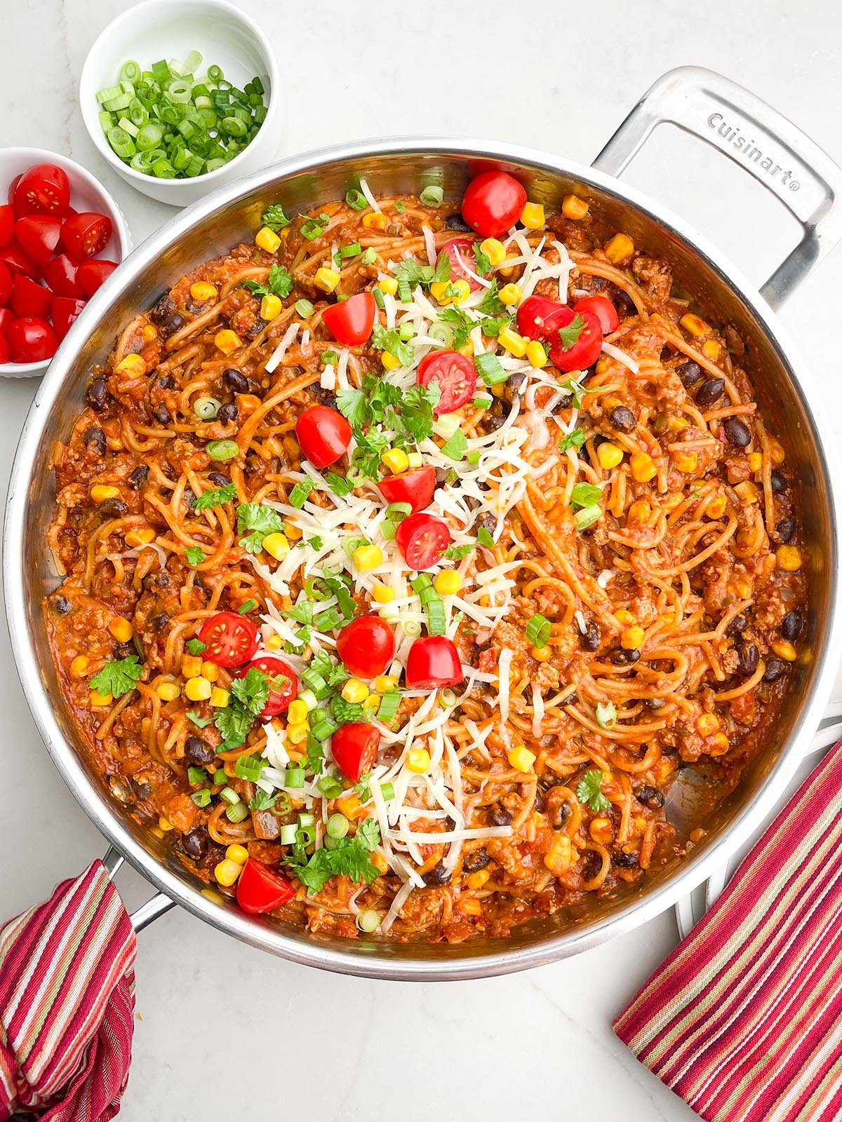 one pot taco spaghetti in skillet with fresh grape tomatoes, corn, green onions and cheese down the middle.