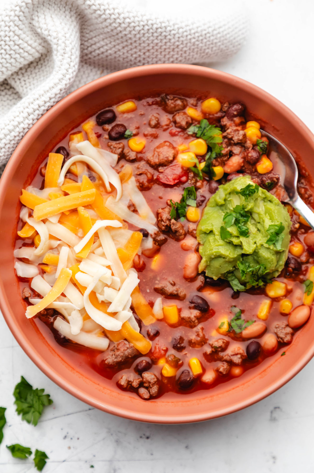 taco soup in a bowl with shredded cheese and guacamole on top.