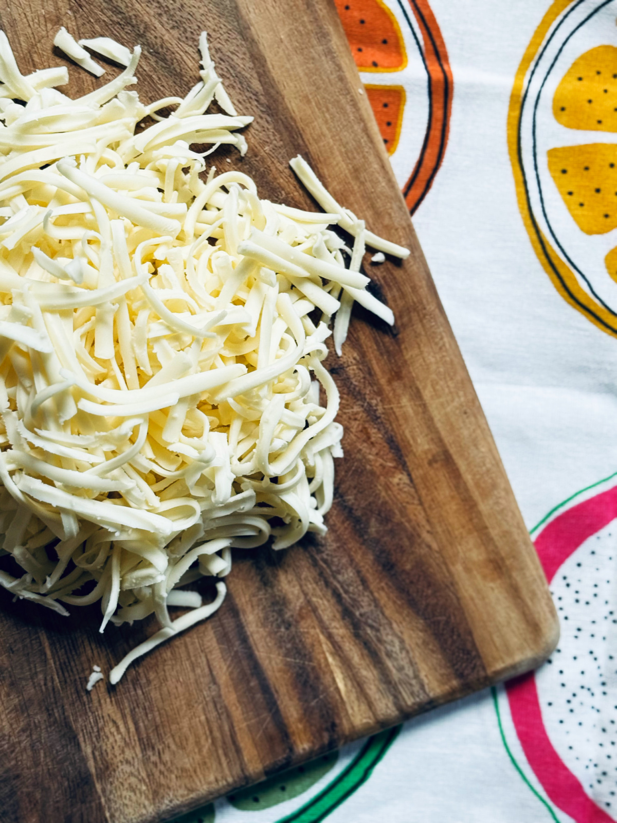 shredded monterey jack cheese on cutting board on colorful tea towel.