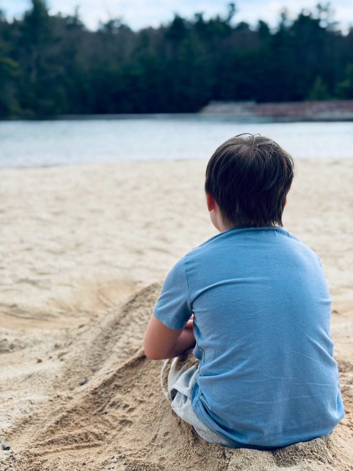 unschooled child covered in sand sitting by lake.