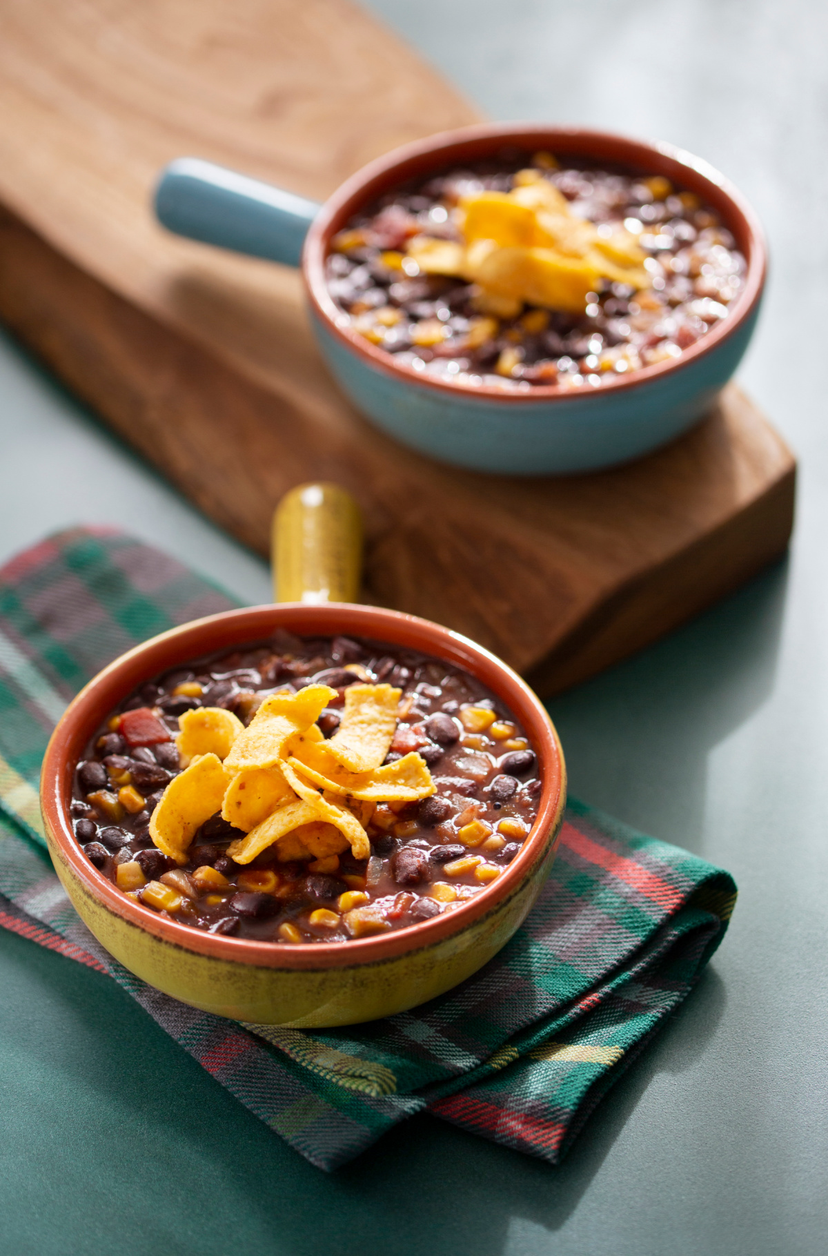 two crocks of black bean corn soup on plaid napkins and cutting board.