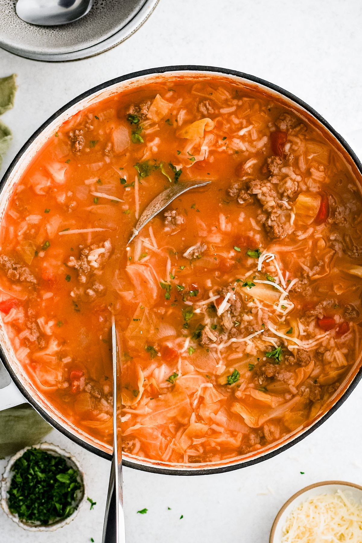 cabbage roll soup in bowl with spoon on countertop with toppings on the side.