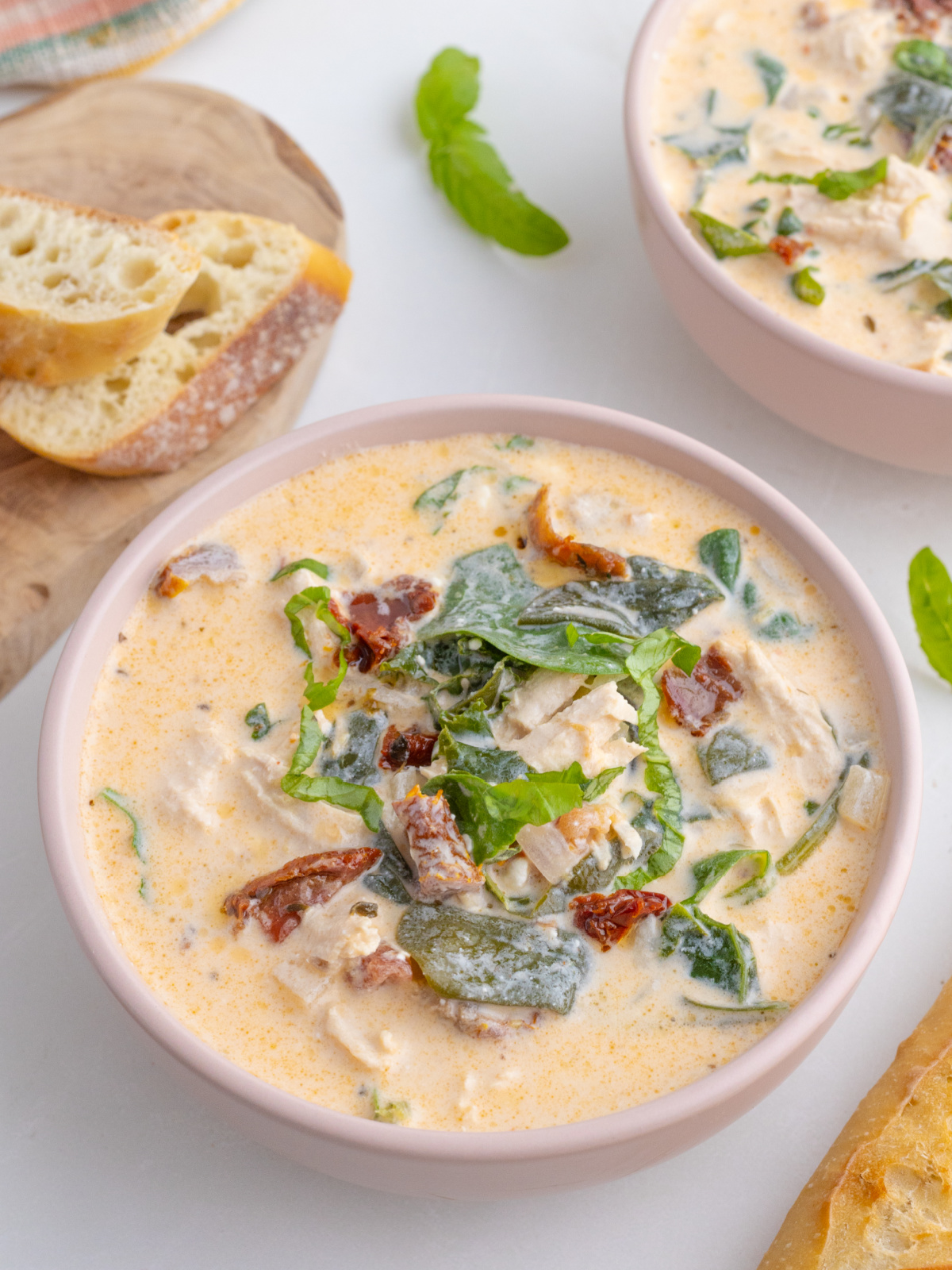 Marry Me Chicken soup in pink bowls with baguette and basil leaves nearby
