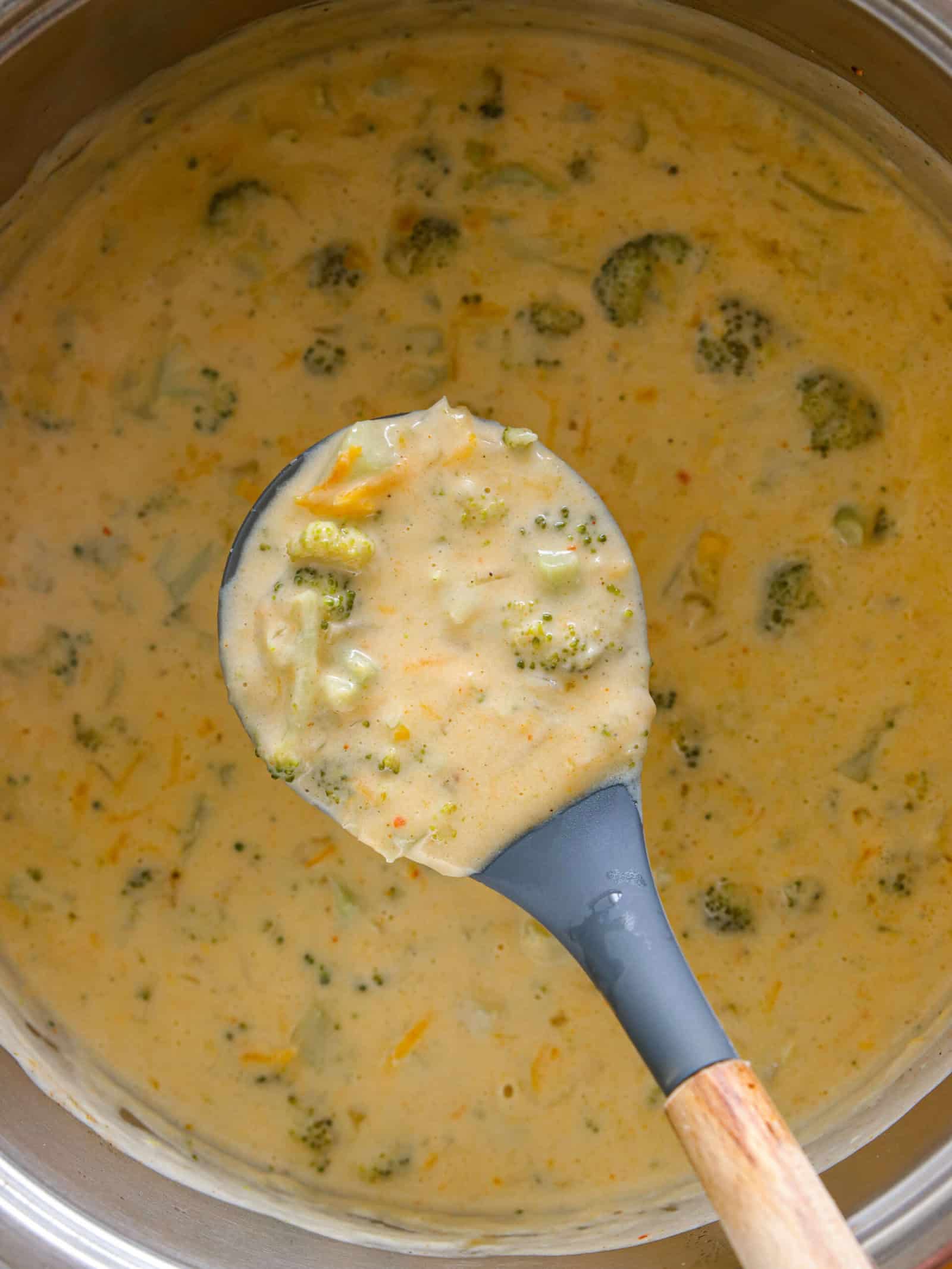broccoli cheddar soup in pot with close up of cooking ladle holding a spoonful.