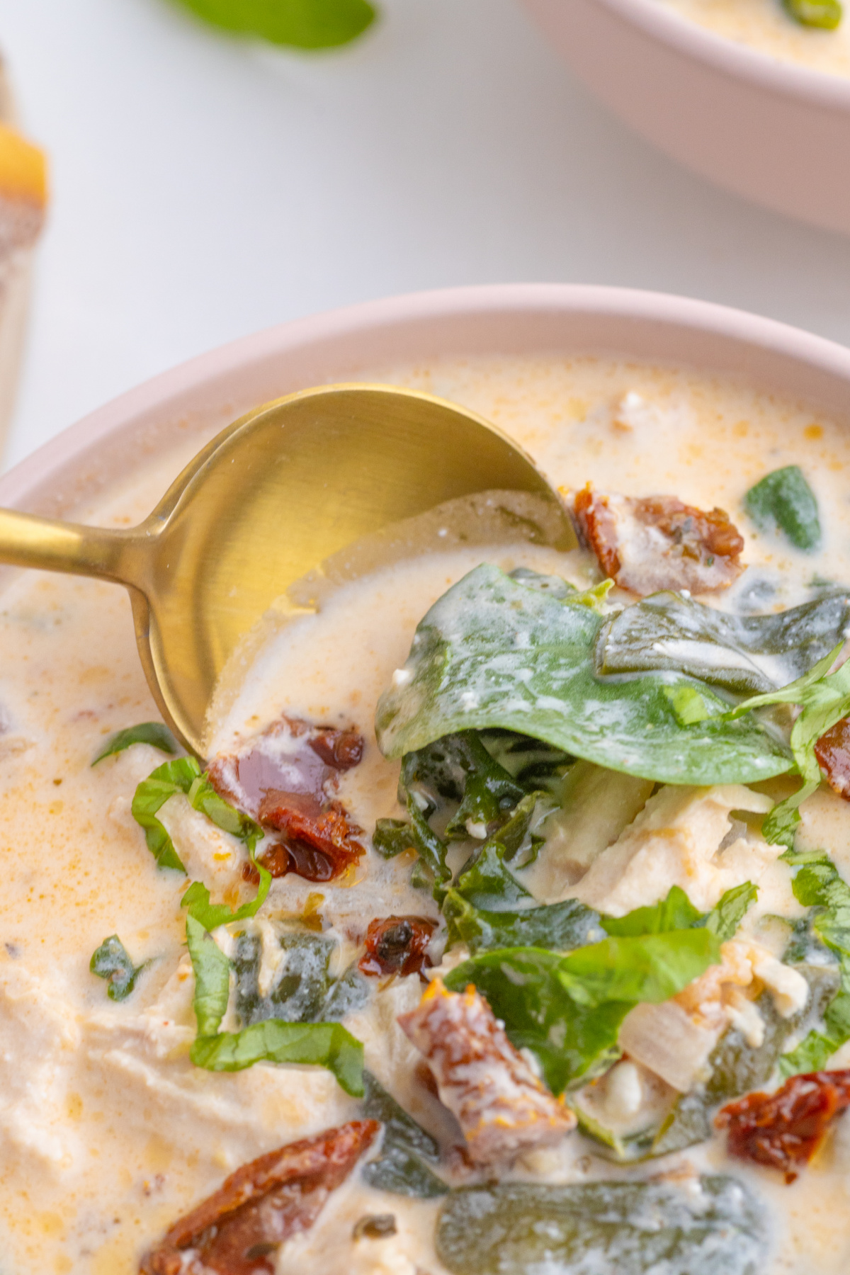 creamy chicken soup in pink bowl with gold spoon stirring.