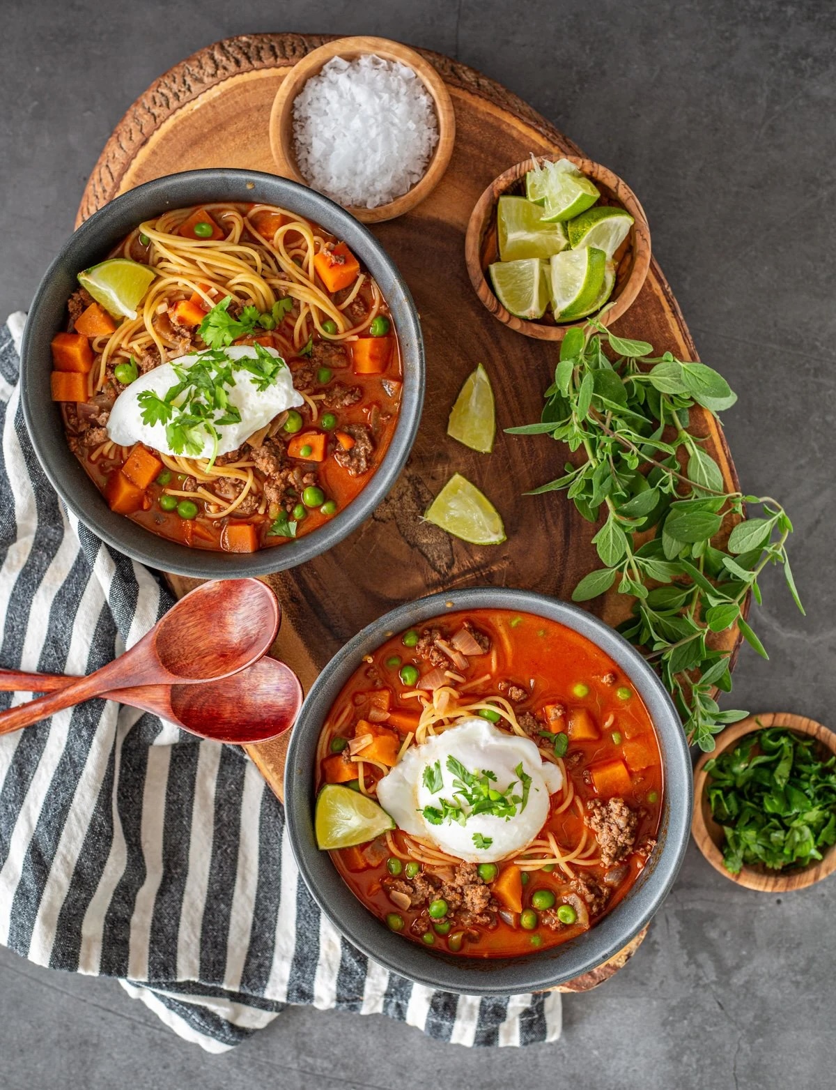 bowls of Peruvian beef noodle soup on cutting board with limes, coconut flakes and cilantro.