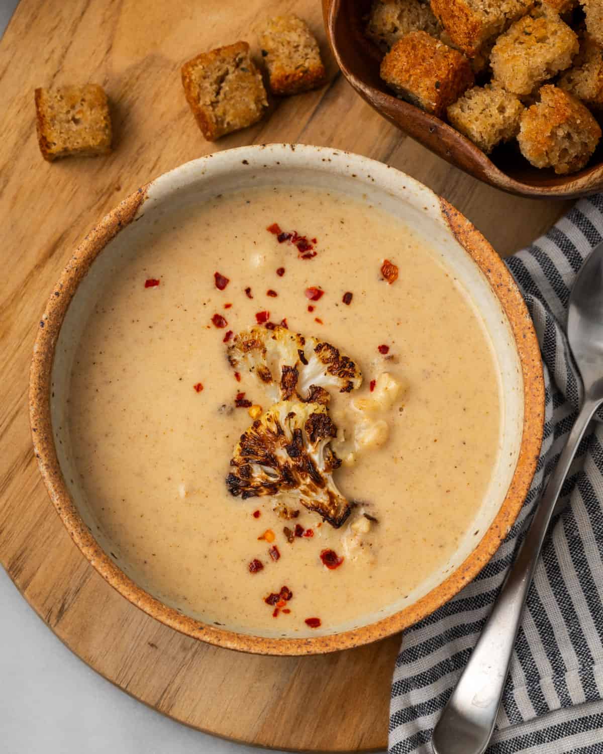 cauliflower soup topped with red pepper flakes in pottery bowl and croutons on the side.
