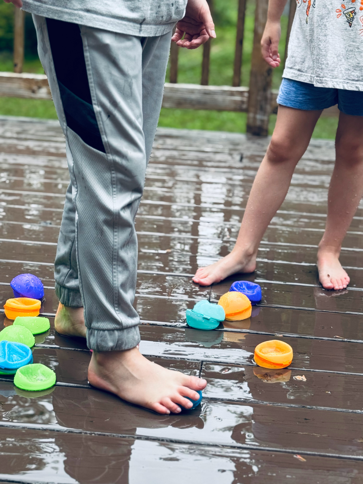 children's feet around reusable water balloons on deck, cheap activities to afford to homeschool concept.