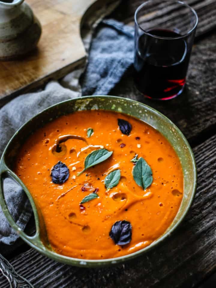 homemade tomato soup topped with fresh basil leaves in green pottery bowl.