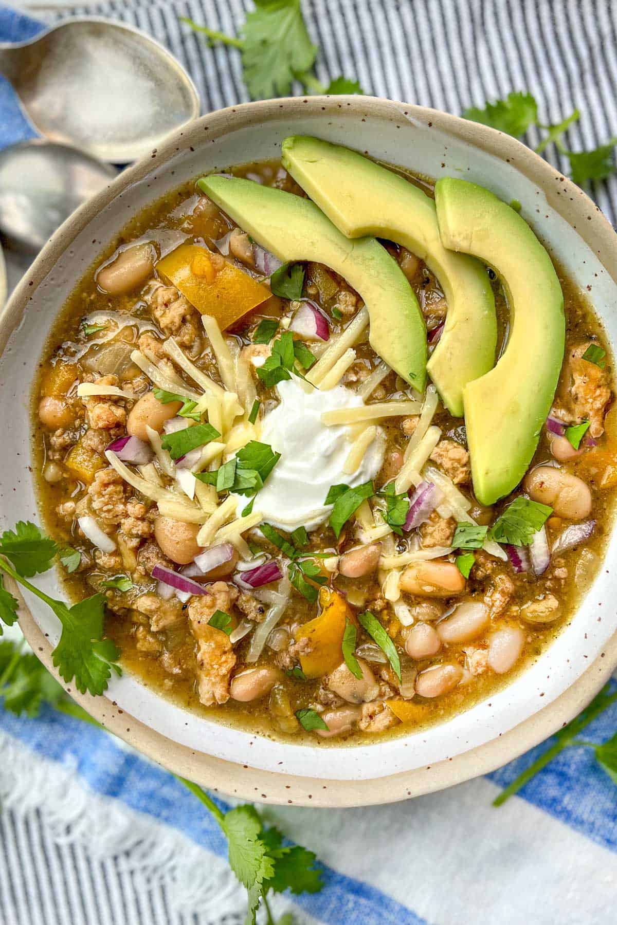 white bean turkey chili in bowl, topped with avocado slices, shredded cheese and sour cream.