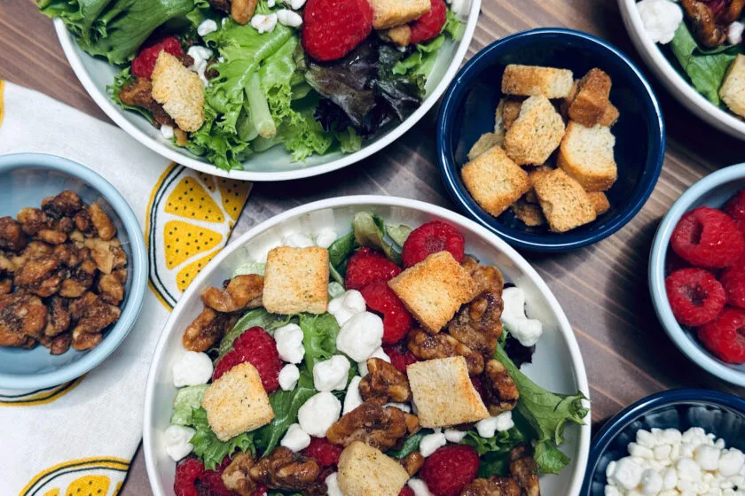 raspberry walnut salads individual servings in white bowls surrounded by ingredients in small bowls.