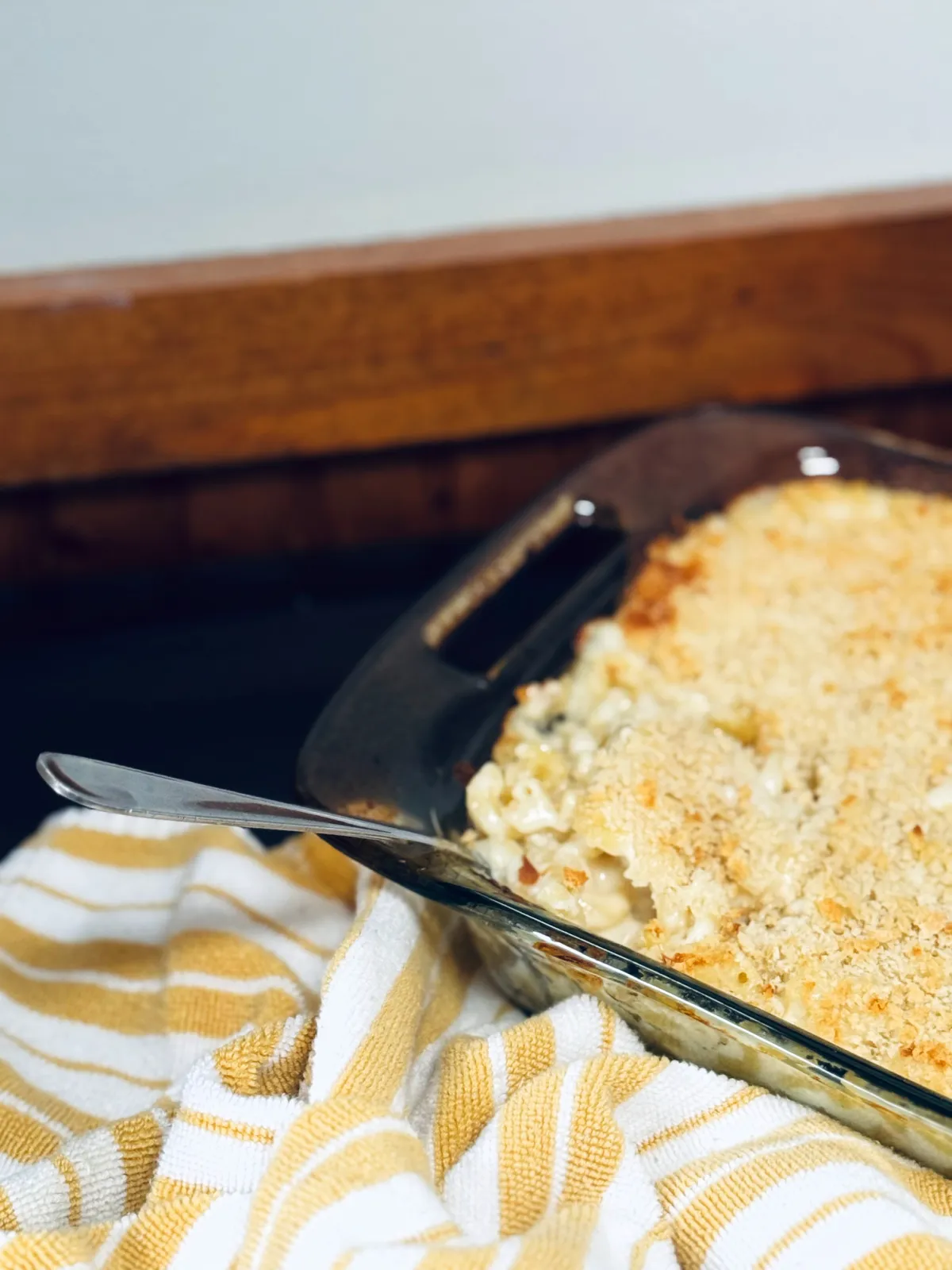 Grandma's baked mac and cheese in casserole dish with serving spoon and yellow and white striped towel nearby.