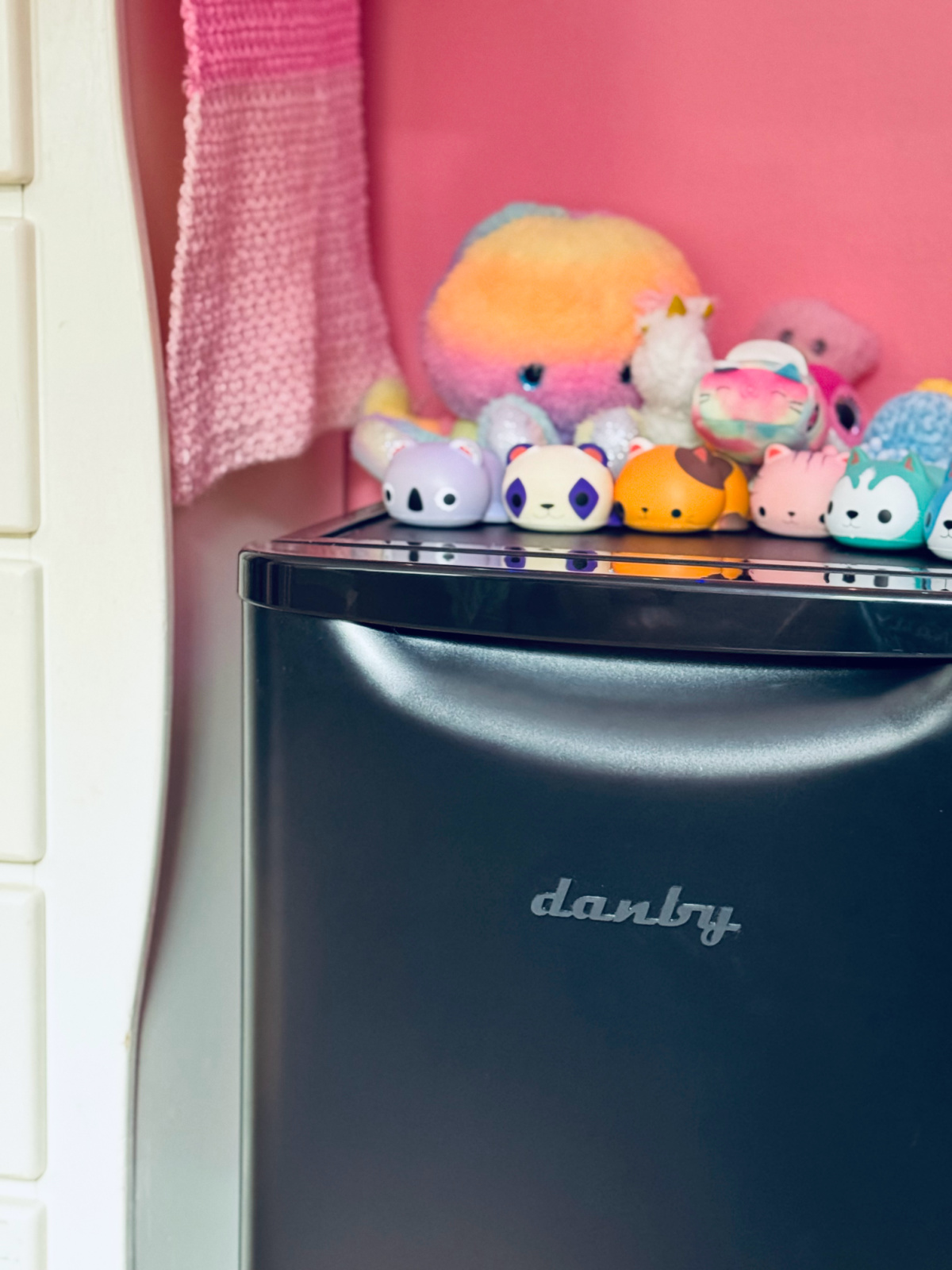 black danby mini fridge with stuffed animals on top and pink wall background.