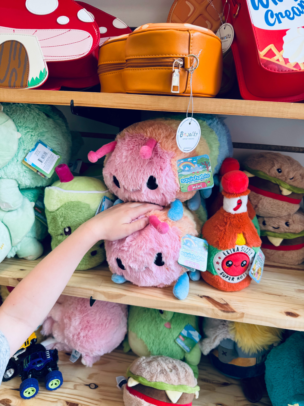 toy shelves full of colorful stuffed animal toys with child touching a pink fluffy one.