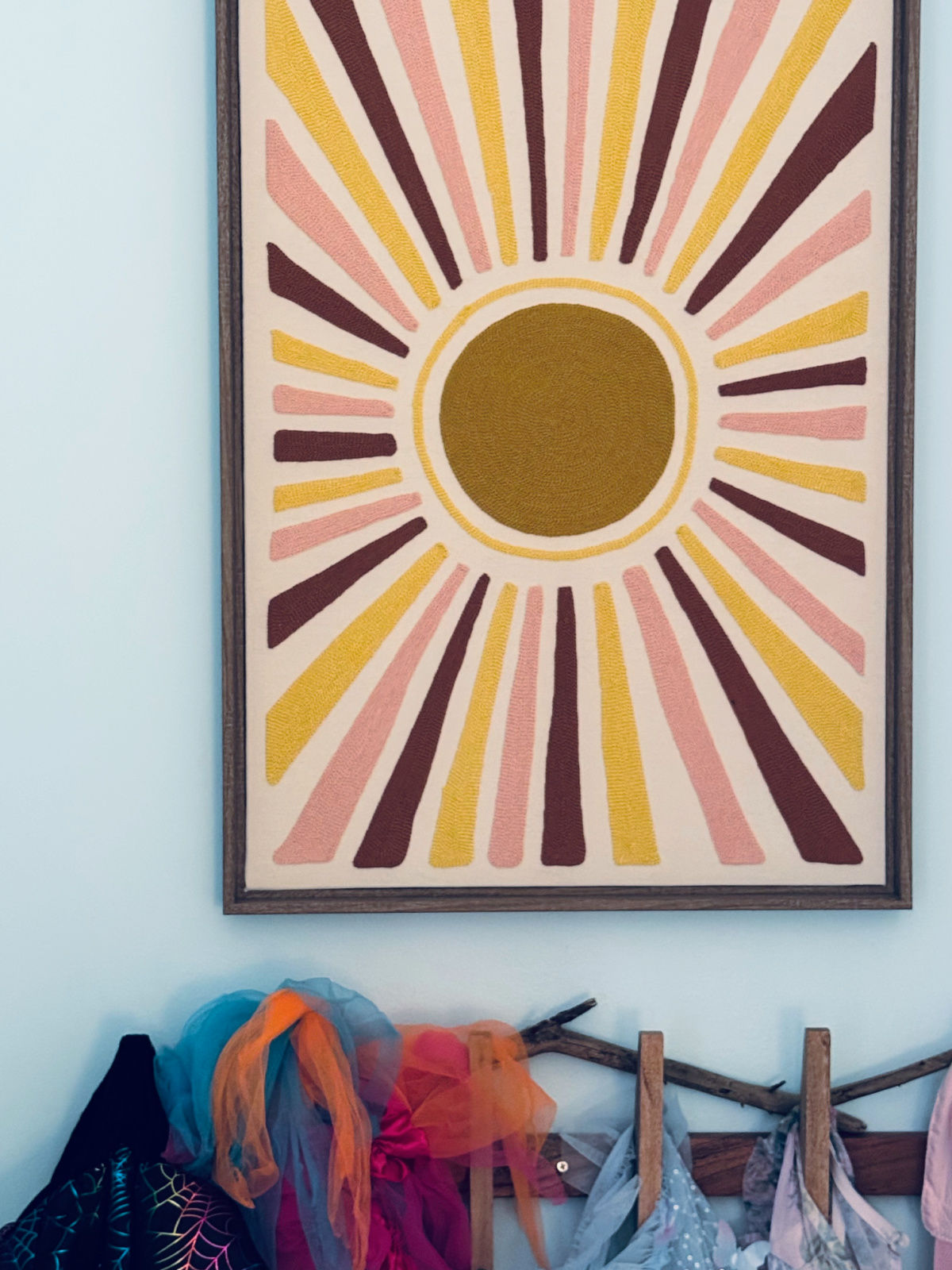embroidered sun wall art above clothing rack.