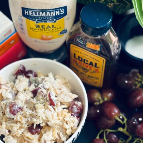 chicken salad in bowl with honey, mayonnaise, books, and grapes in background.