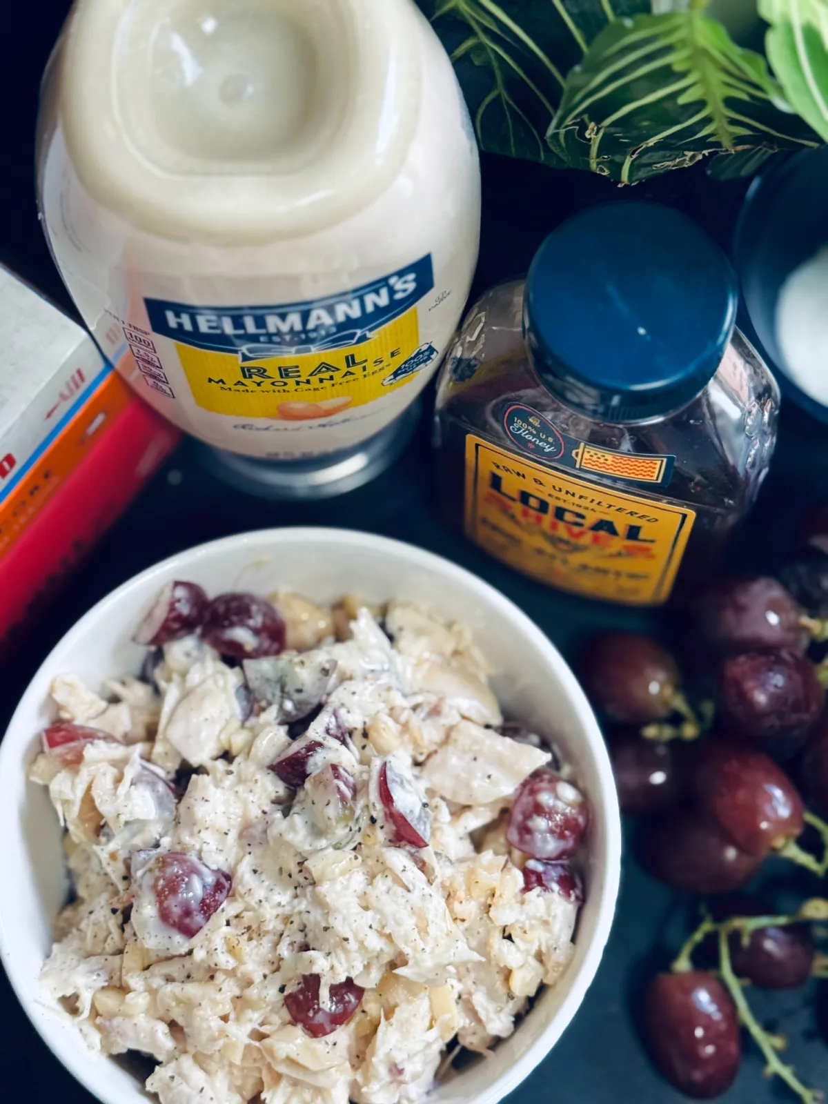 rotisserie chicken salad in bowl with honey, mayo and grapes nearby.