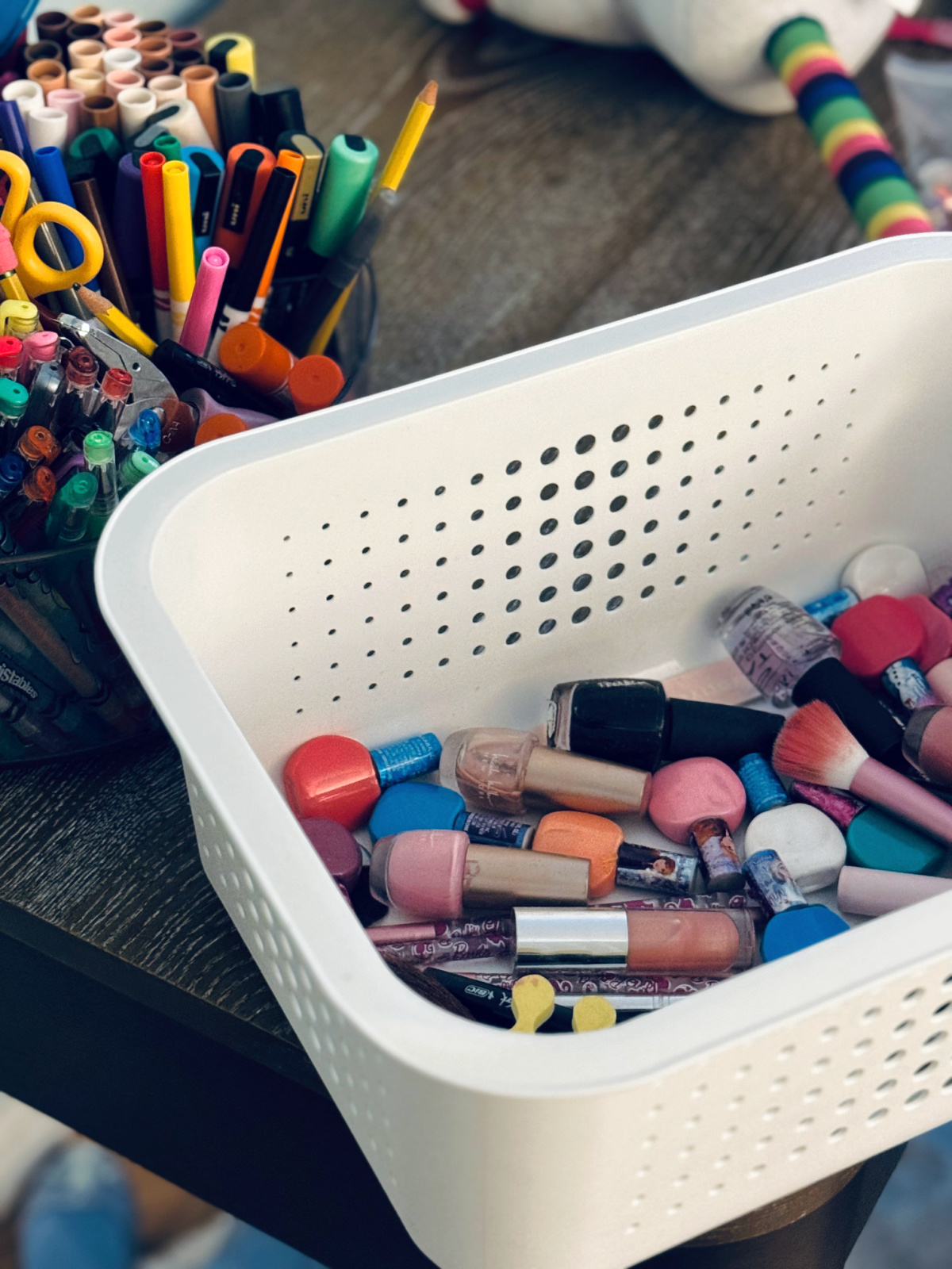 white organization bin with nail polish and makeup, sitting on desk near lazy susan with colorful markers.