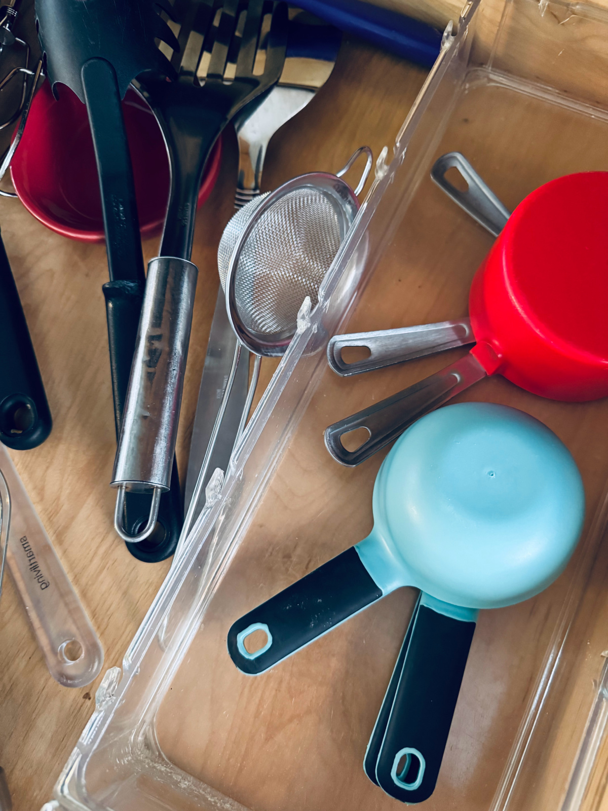 two sets of colorful measuring cups in drawer with multiple spatulas.