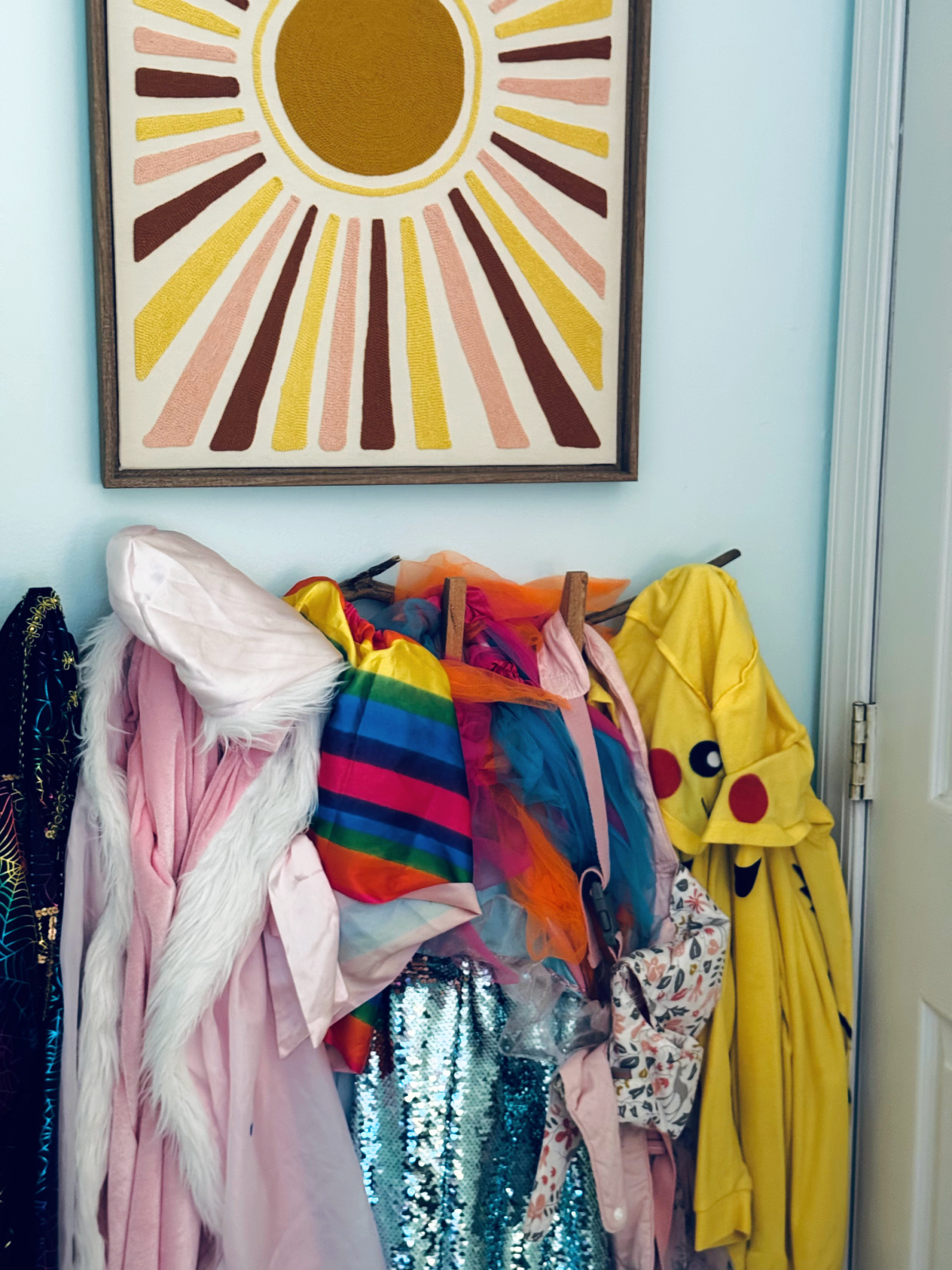 wall hooks with colorful articles of clothing and dress-up, below colorful sunburst artwork.