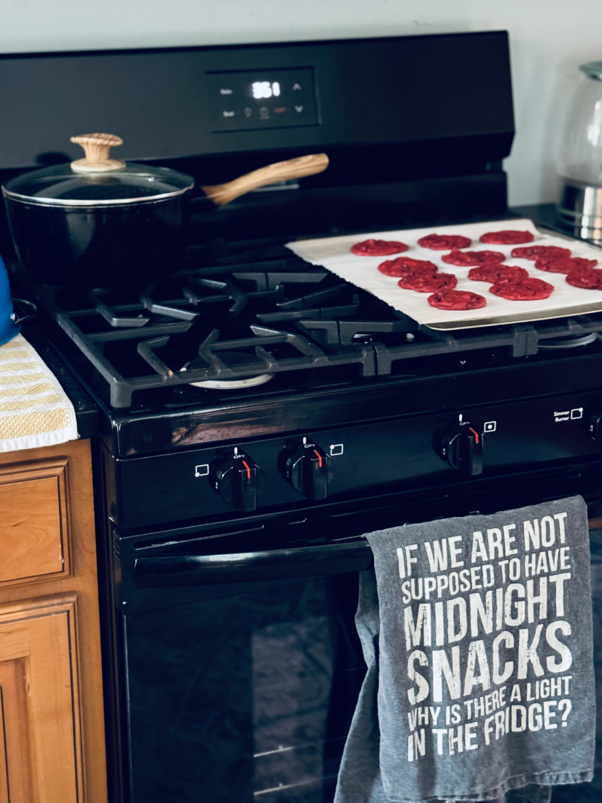 black oven with tea towel hanging, cookies on tray and saucepan on stovetop.
