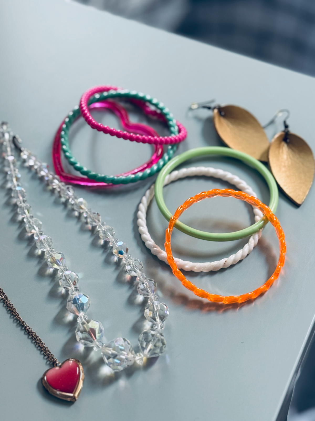 necklaces, bracelets and earrings laid out on light green metal cabinet.