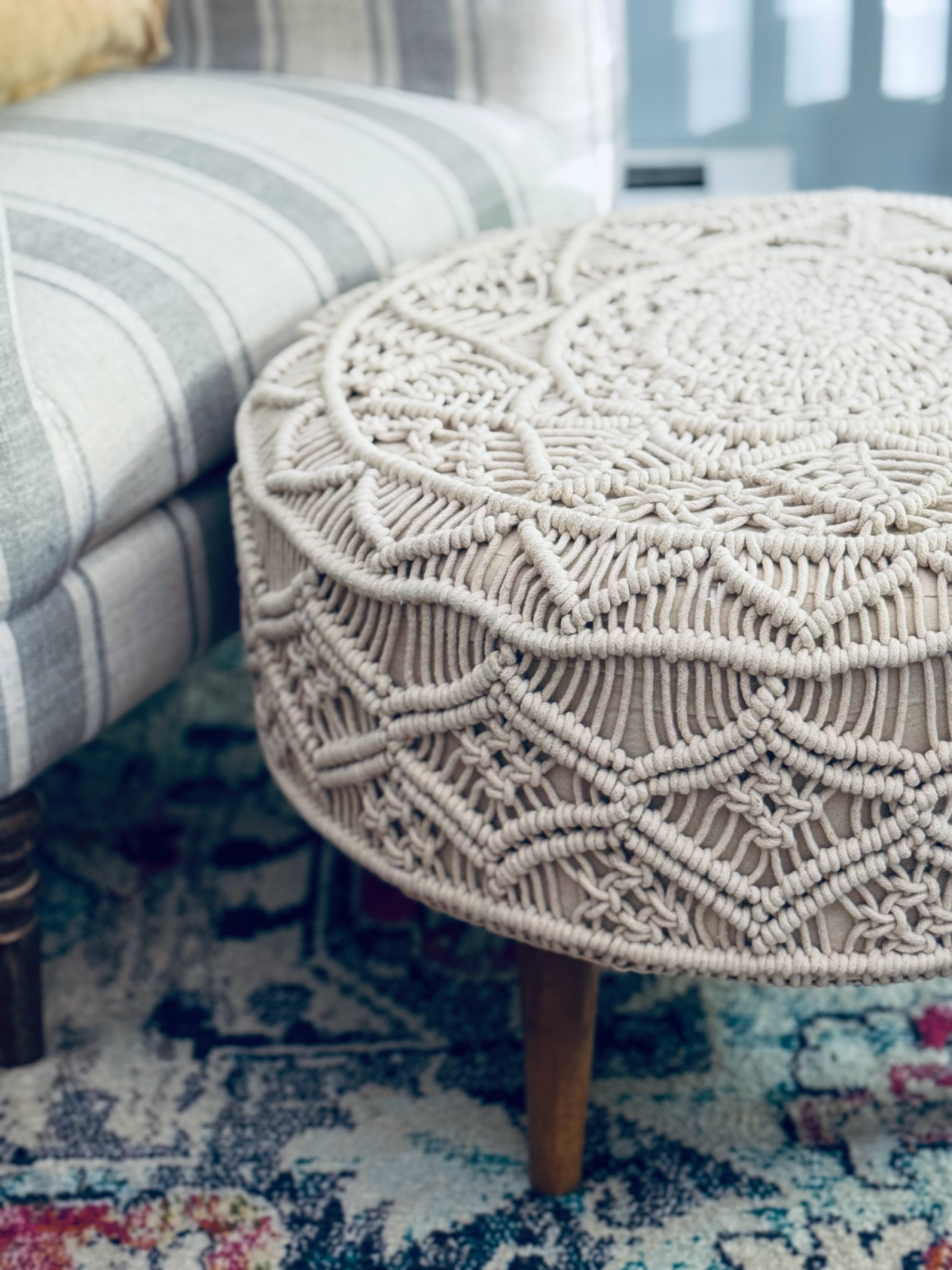 off-white macrame ottoman in front of gray and white striped chair.