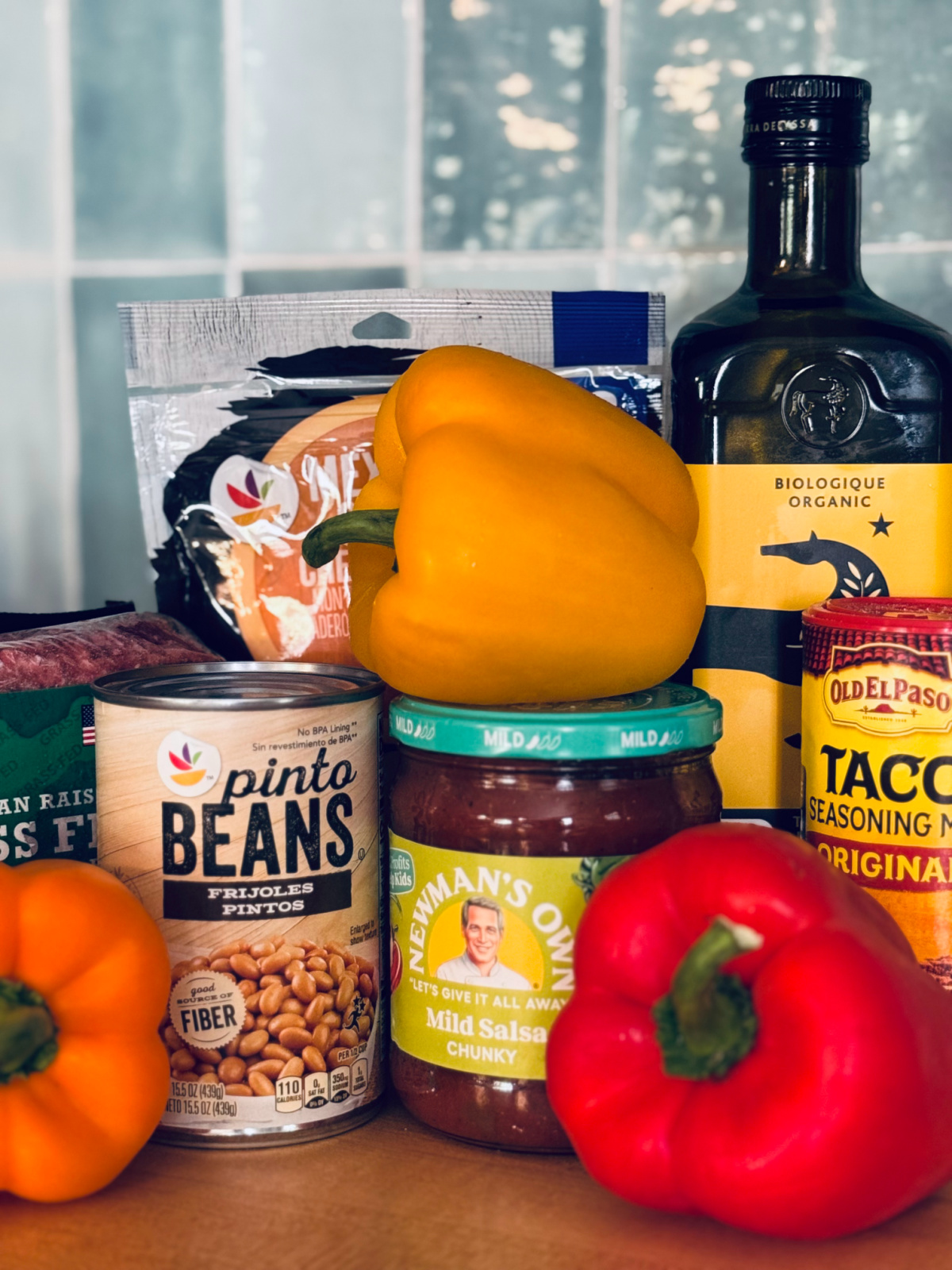 peppers, taco seasoning, salsa, pinto beans, olive oil, ground beef and mexican cheese grouped for taco stuffed peppers ingredient picture.