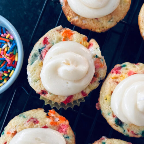 funfetti vanilla cupcakes with store bought vanilla frosting, rainbow sprinkles in light blue ramekin to the side.