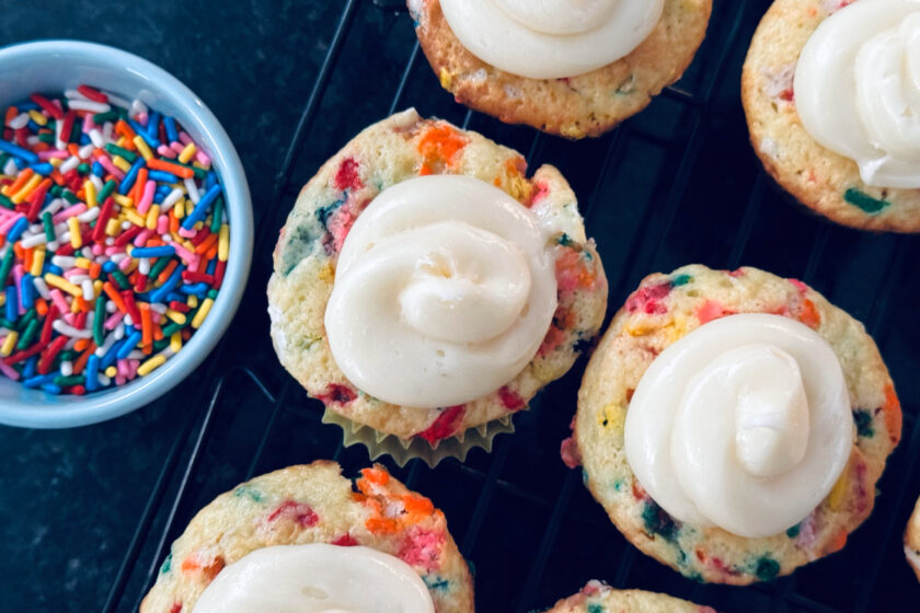 funfetti vanilla cupcakes with store bought vanilla frosting, rainbow sprinkles in light blue ramekin to the side.