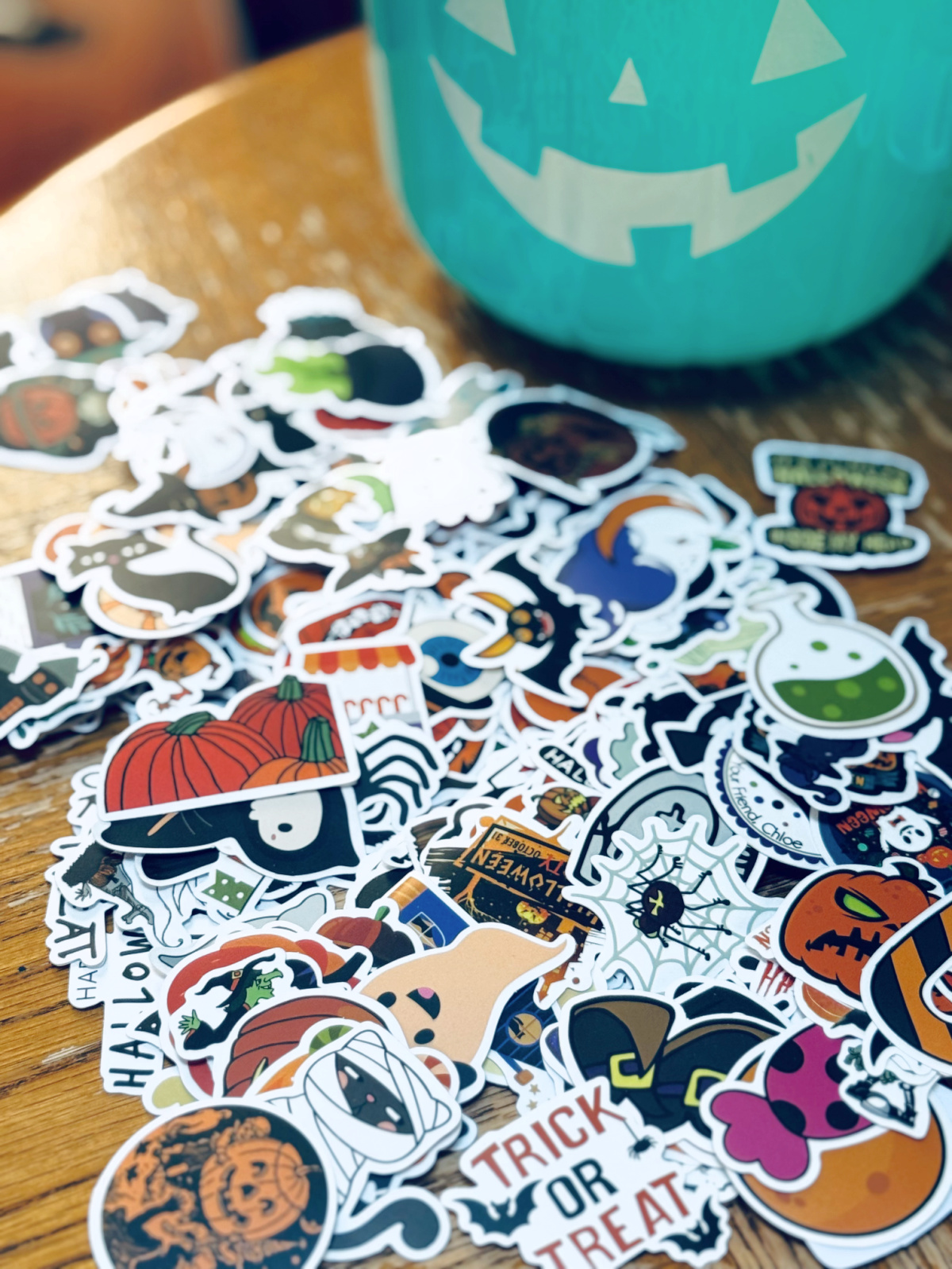 Halloween stickers spread out on table with light blue trick or treating bucket in background.