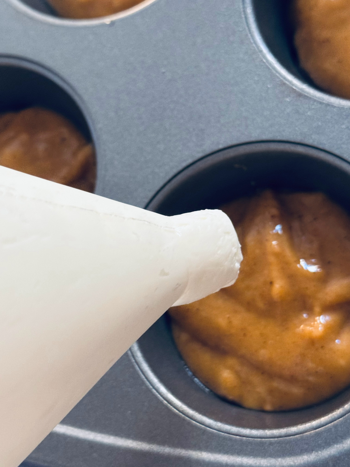 demonstrating how to pipe cream cheese filling into muffin batter.