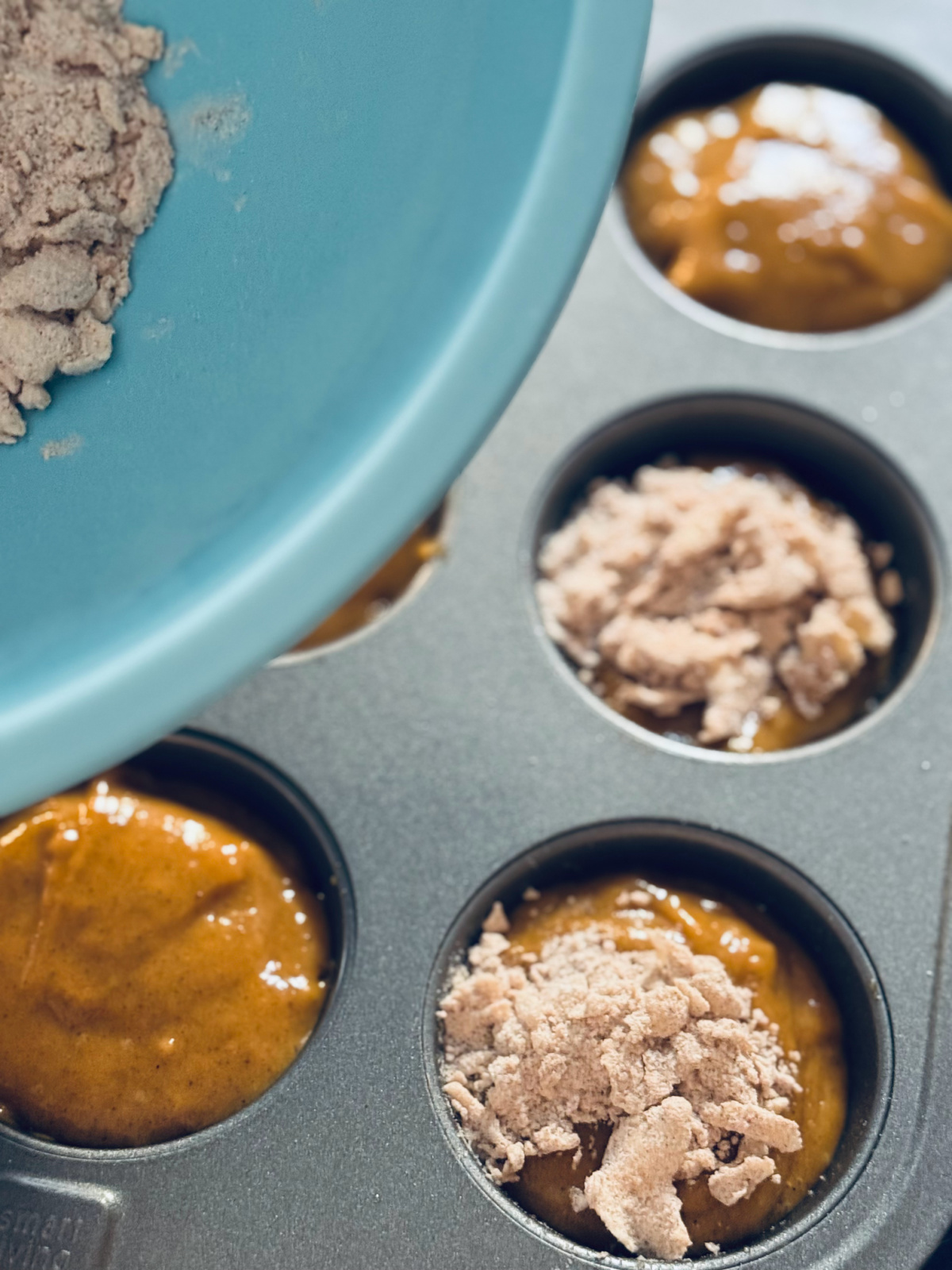 streusel topping on muffin batter with bowl of topping in background.