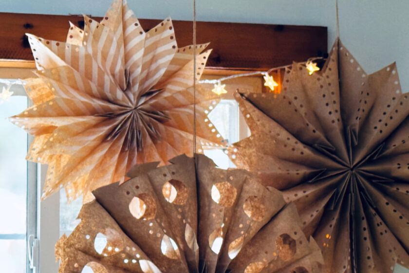 small and large paper bag stars hanging in front of twinkle lights and window.