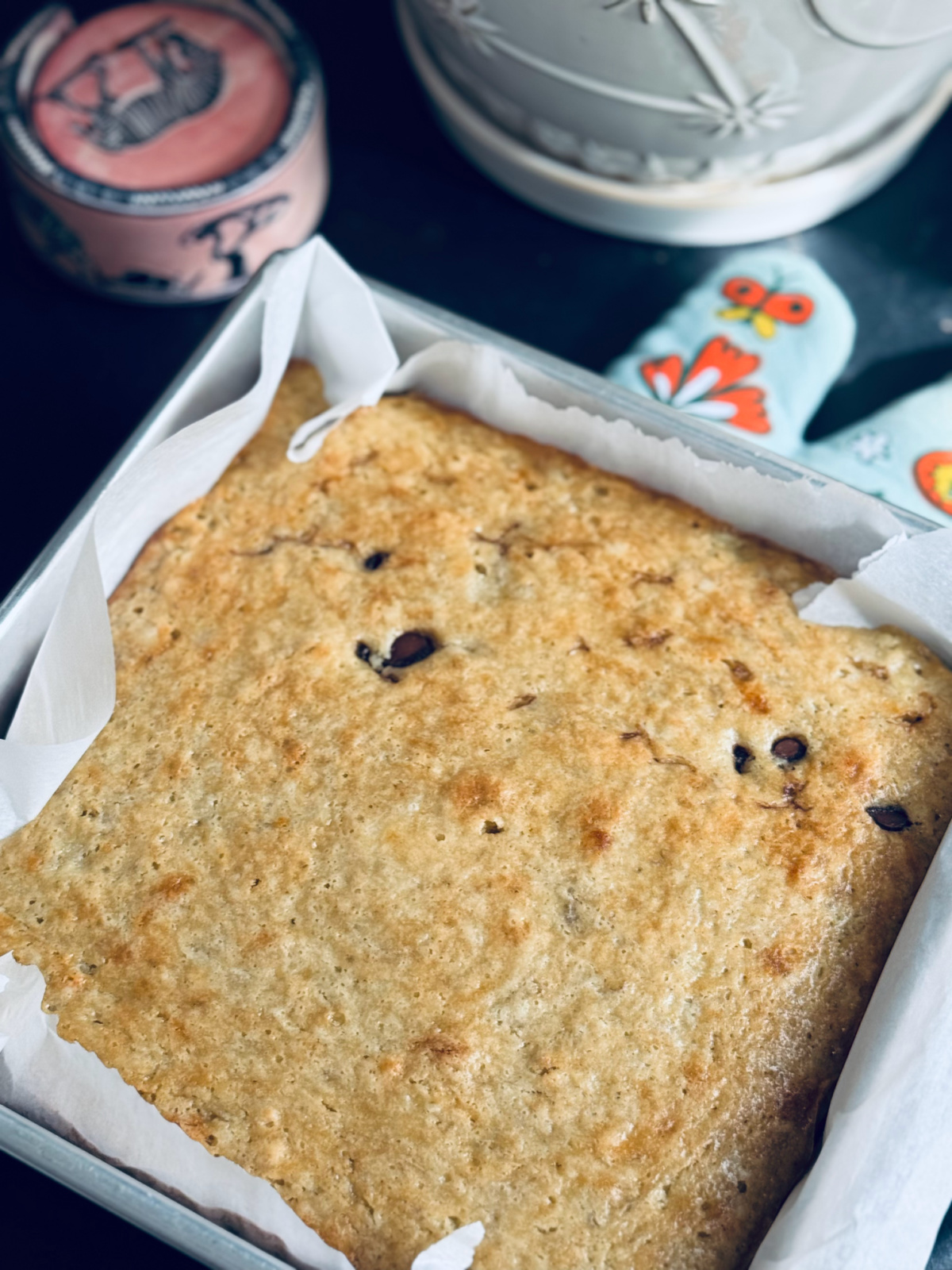 cooked banana bread in square pan with parchment lined paper on colorful oven mitt.