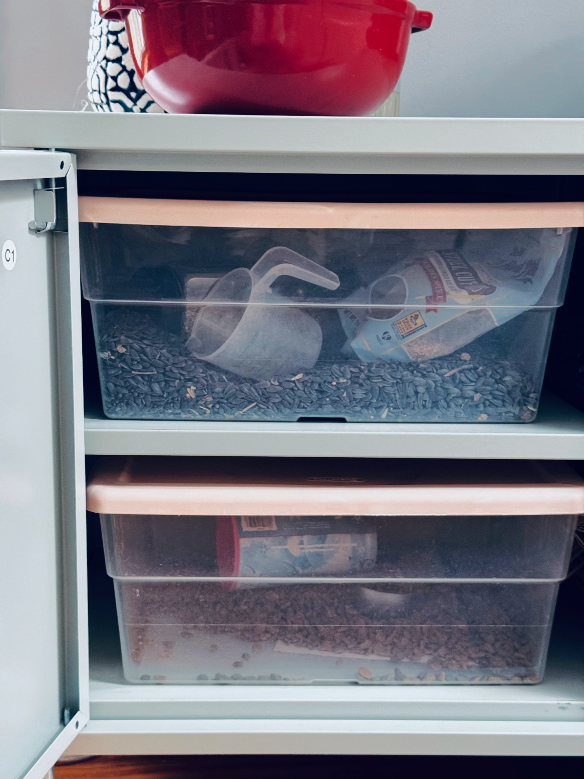 clear plastic containers in metal cabinet, holding bird seed and cat food.