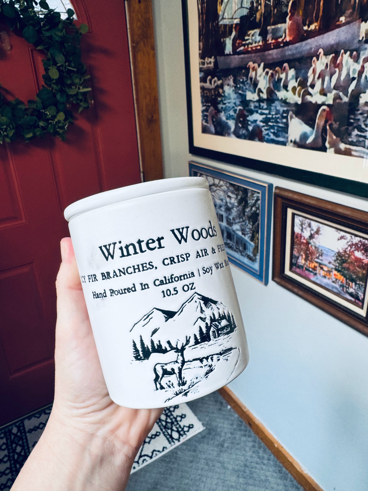 white ceramic candle jar in focus with text "Winter Woods".