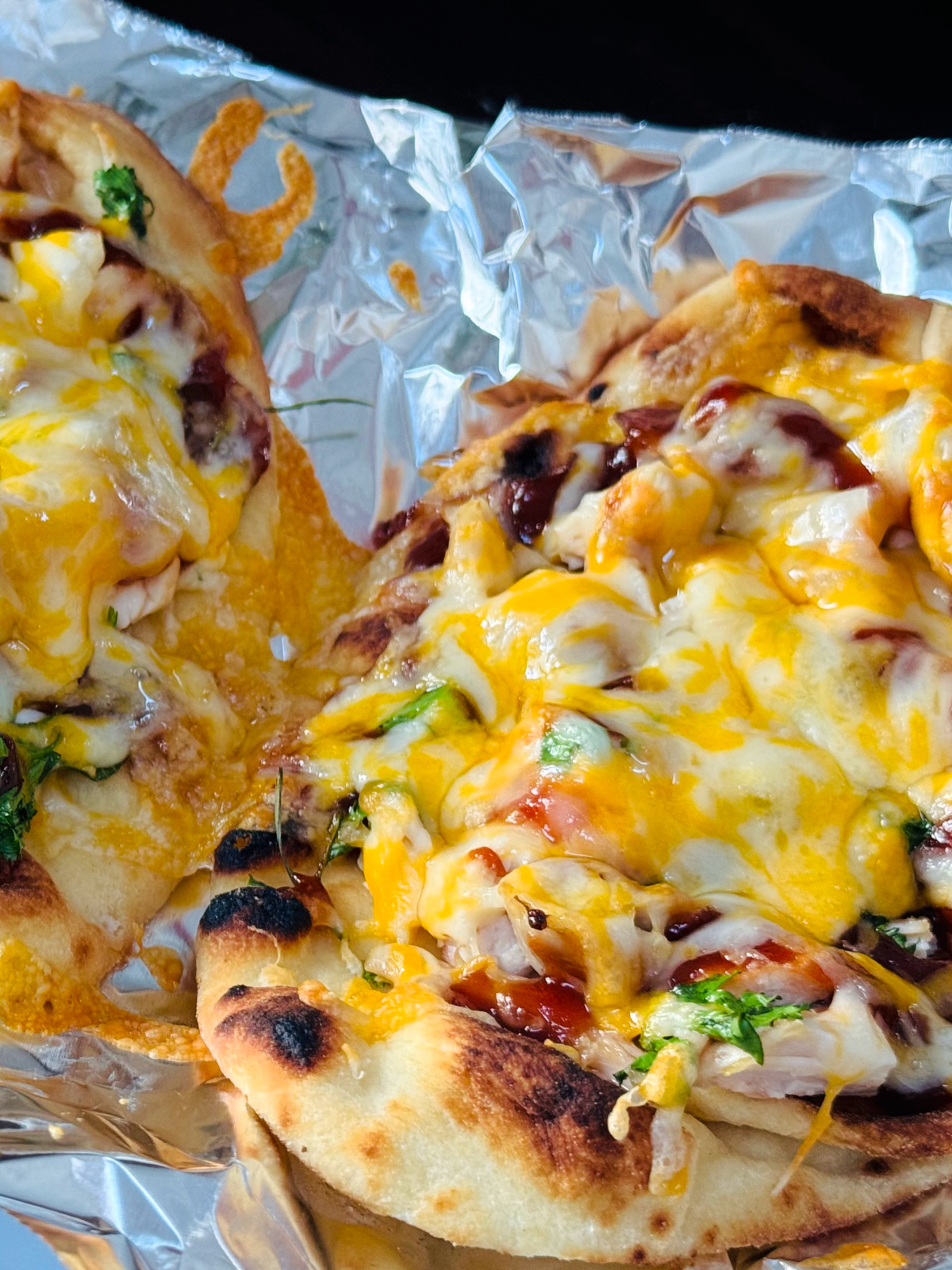 mini bbq chicken naan pizzas on aluminum foil close up.