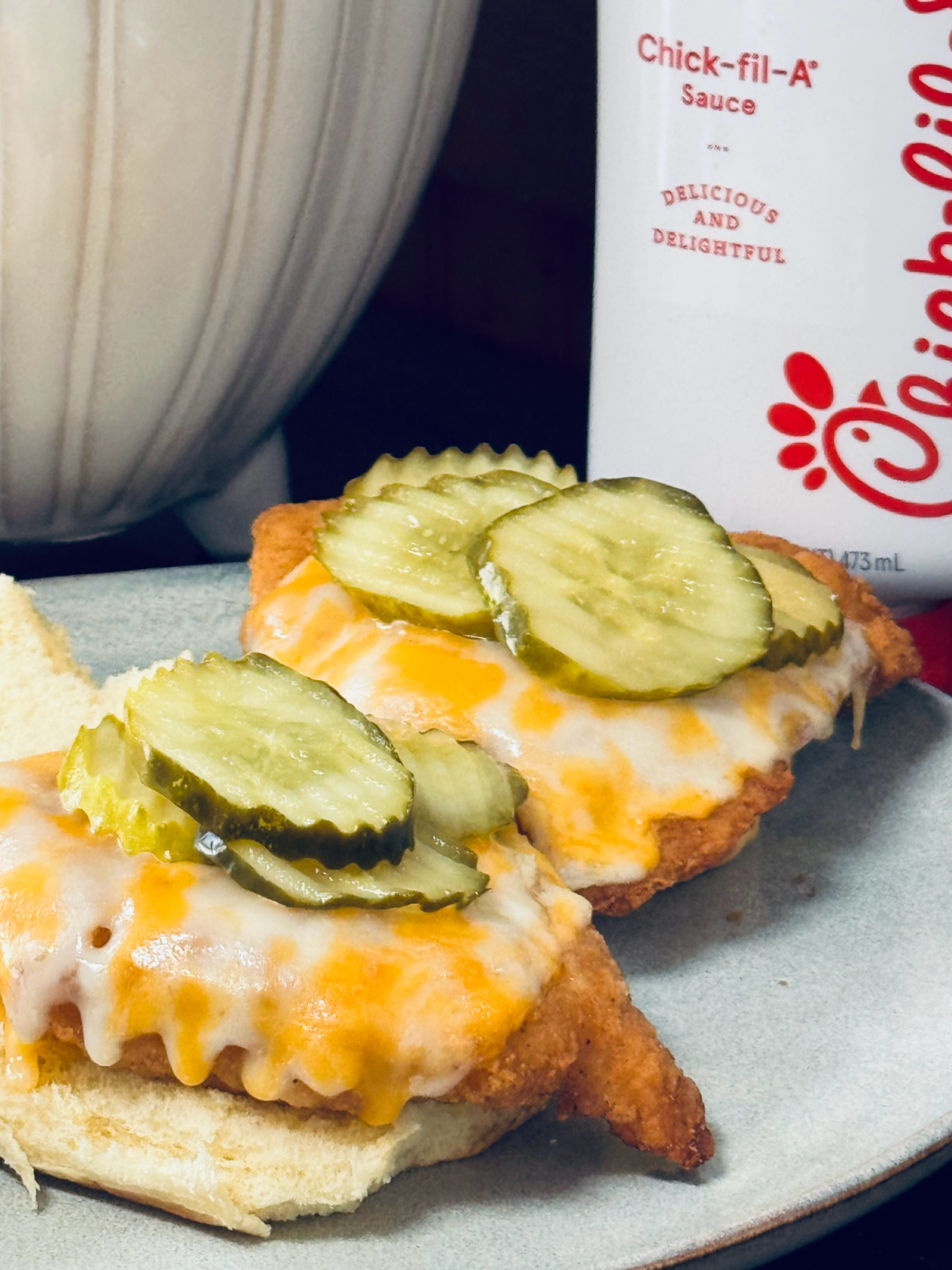 open face chick fil a chicken sandwiches with colby jack cheese and pickles on plate.