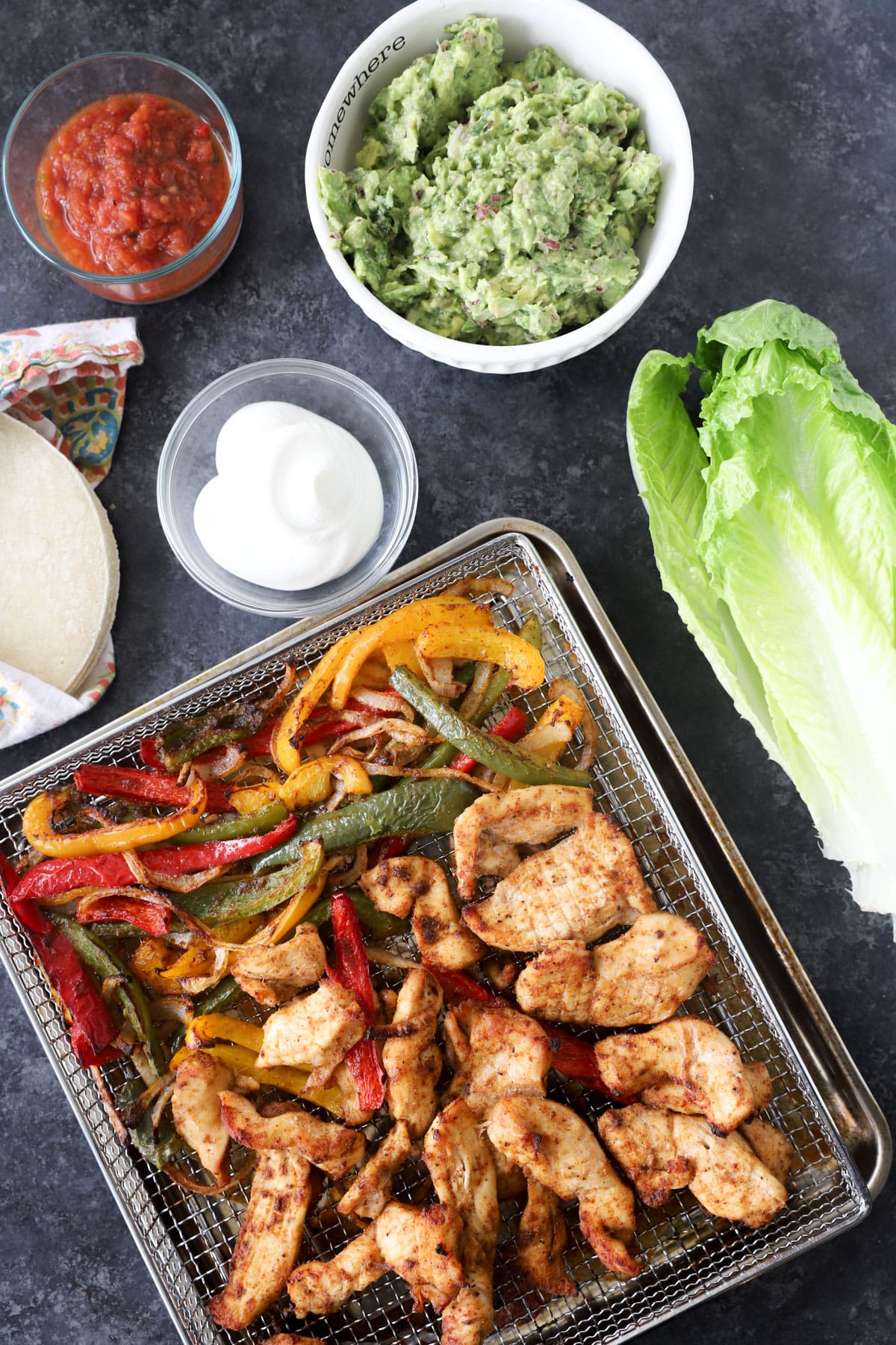 air fryer chicken tacos in air fryer tray surrounded by toppings like guac and sour cream.
