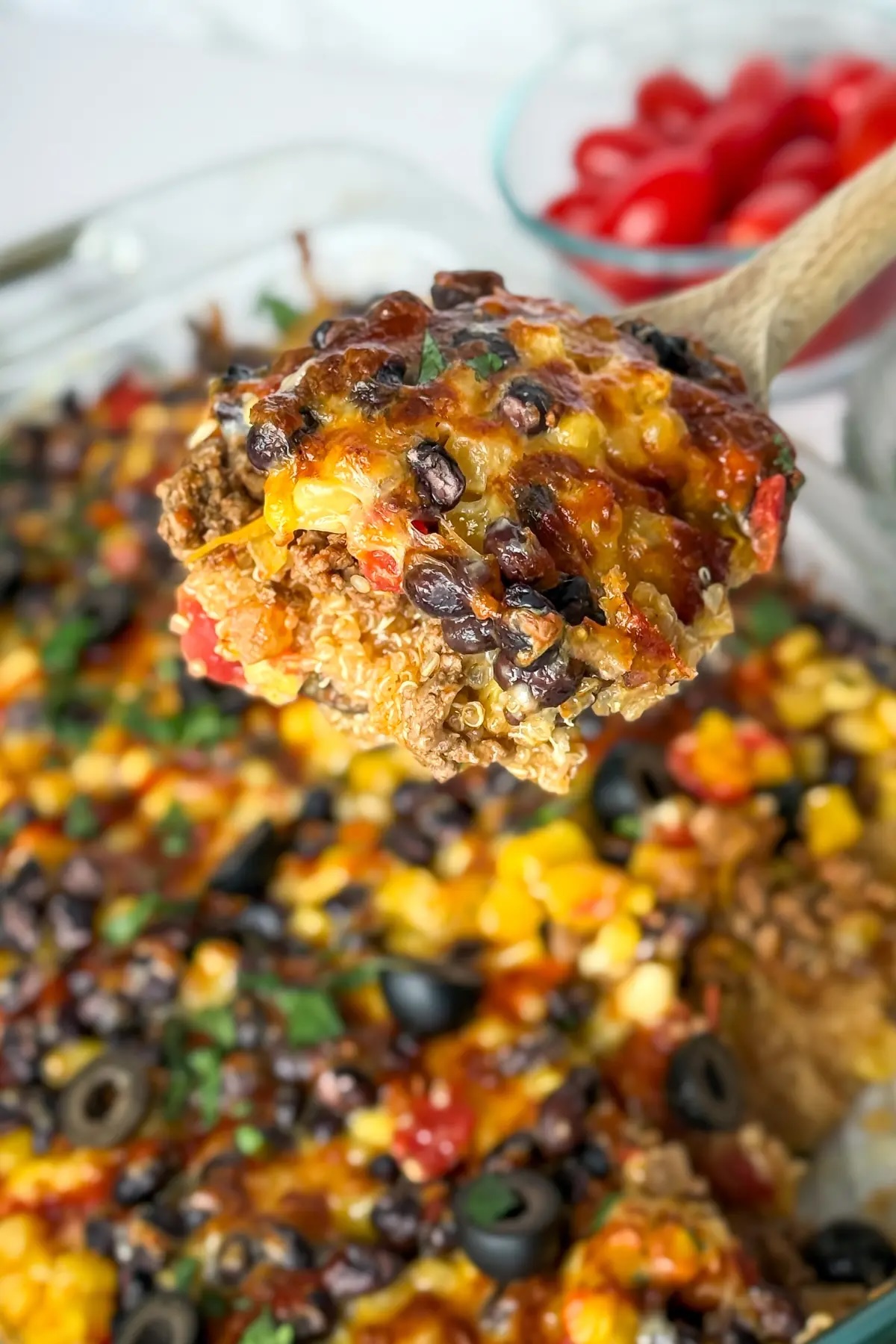 Mexican quinoa casserole with wooden spoon holding a serving over the dish.