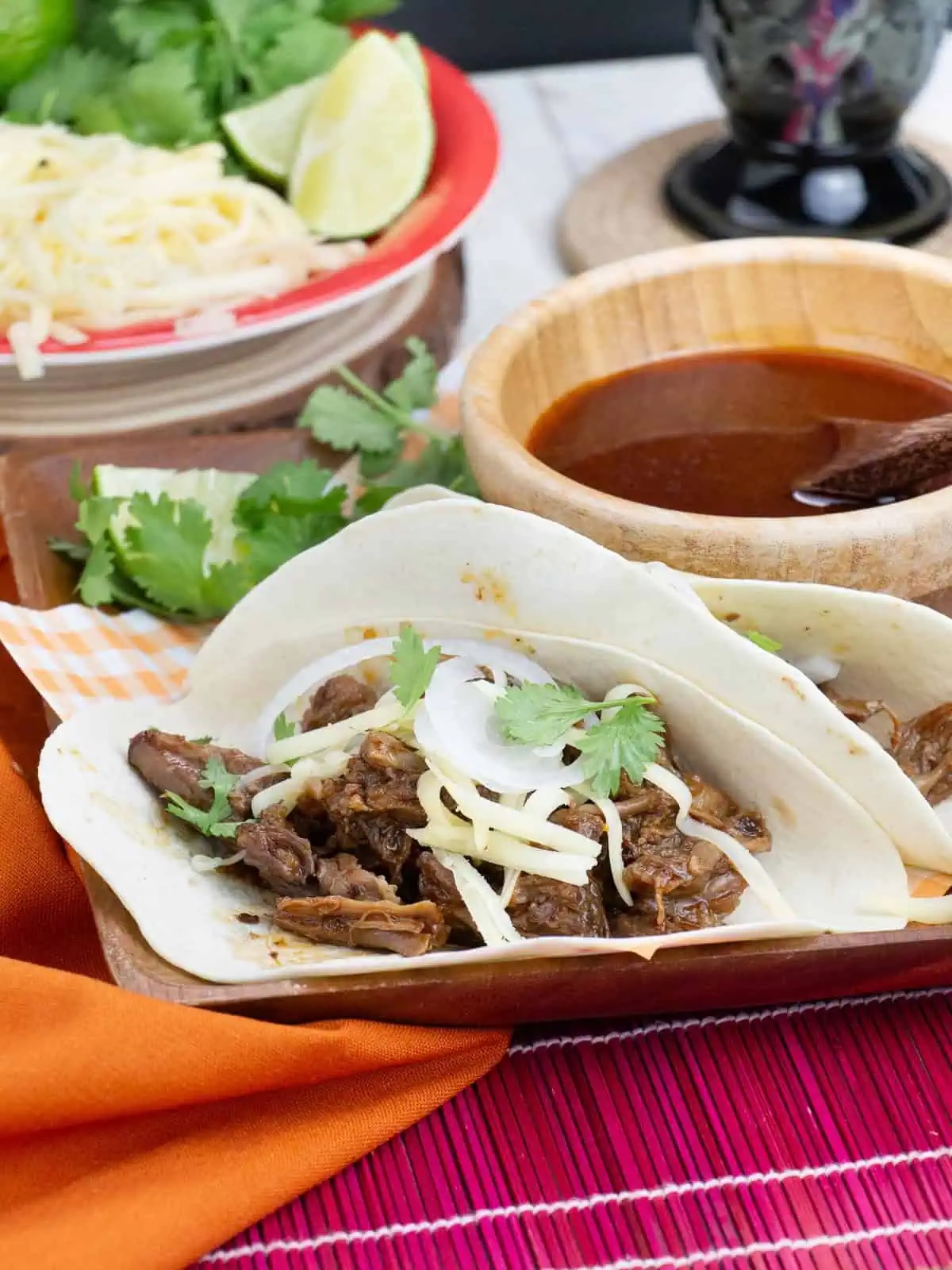 slow-cooked shredded beef tacos assembled with dipping sauce in background.