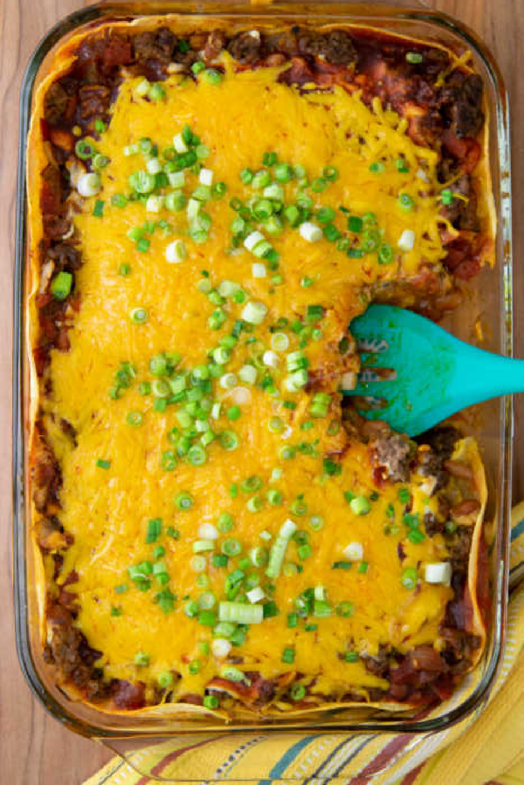 beef enchilada casserole in glass casserole dish topped with cheese and scallions.