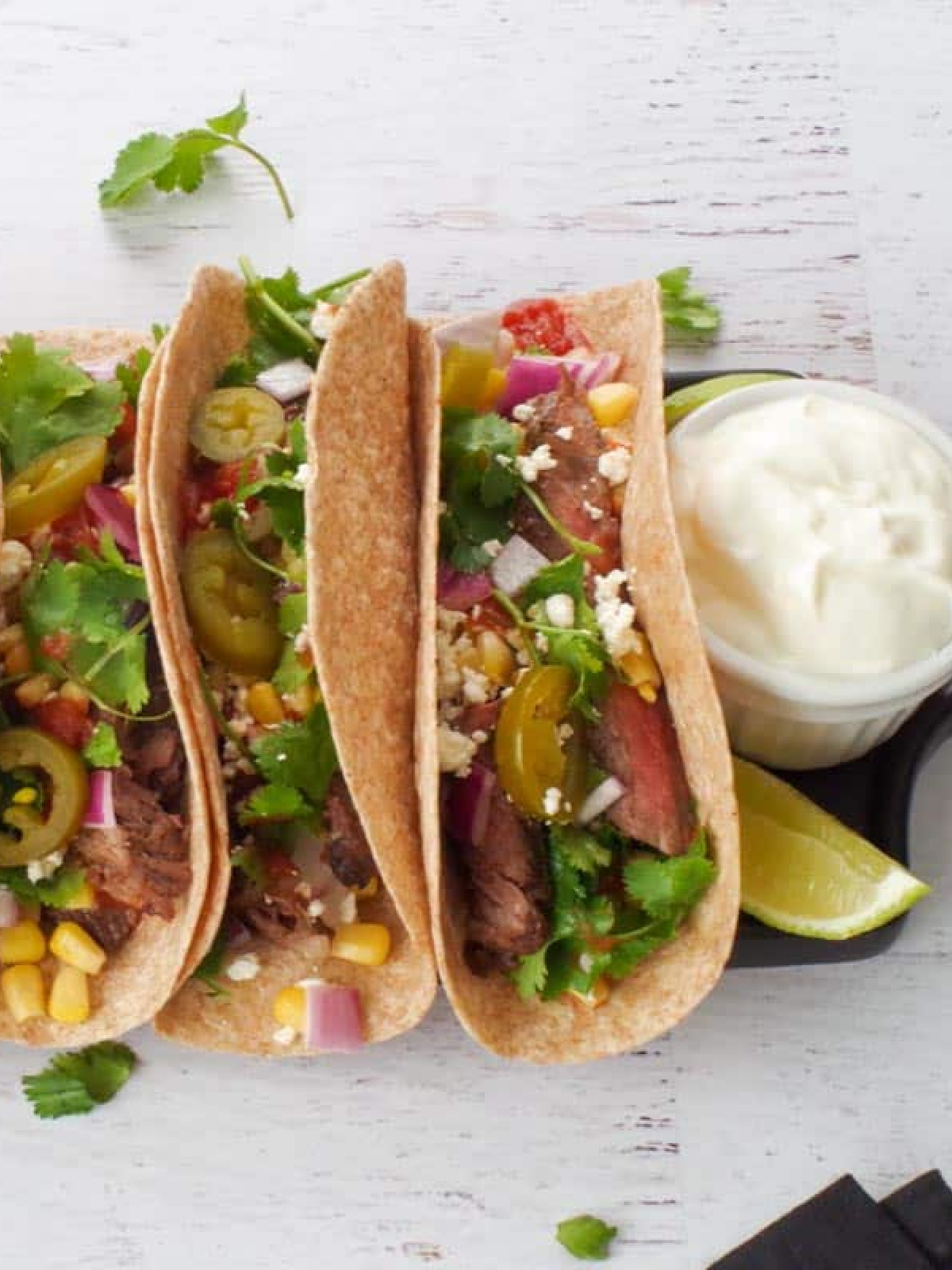 air fryer steak tacos with toppings on tray with sour cream in ramekin nearby.