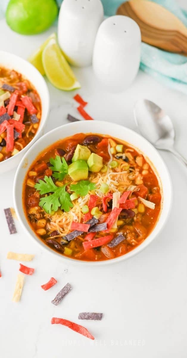 Lazy mom taco soup in bowl with toppings on white surface.