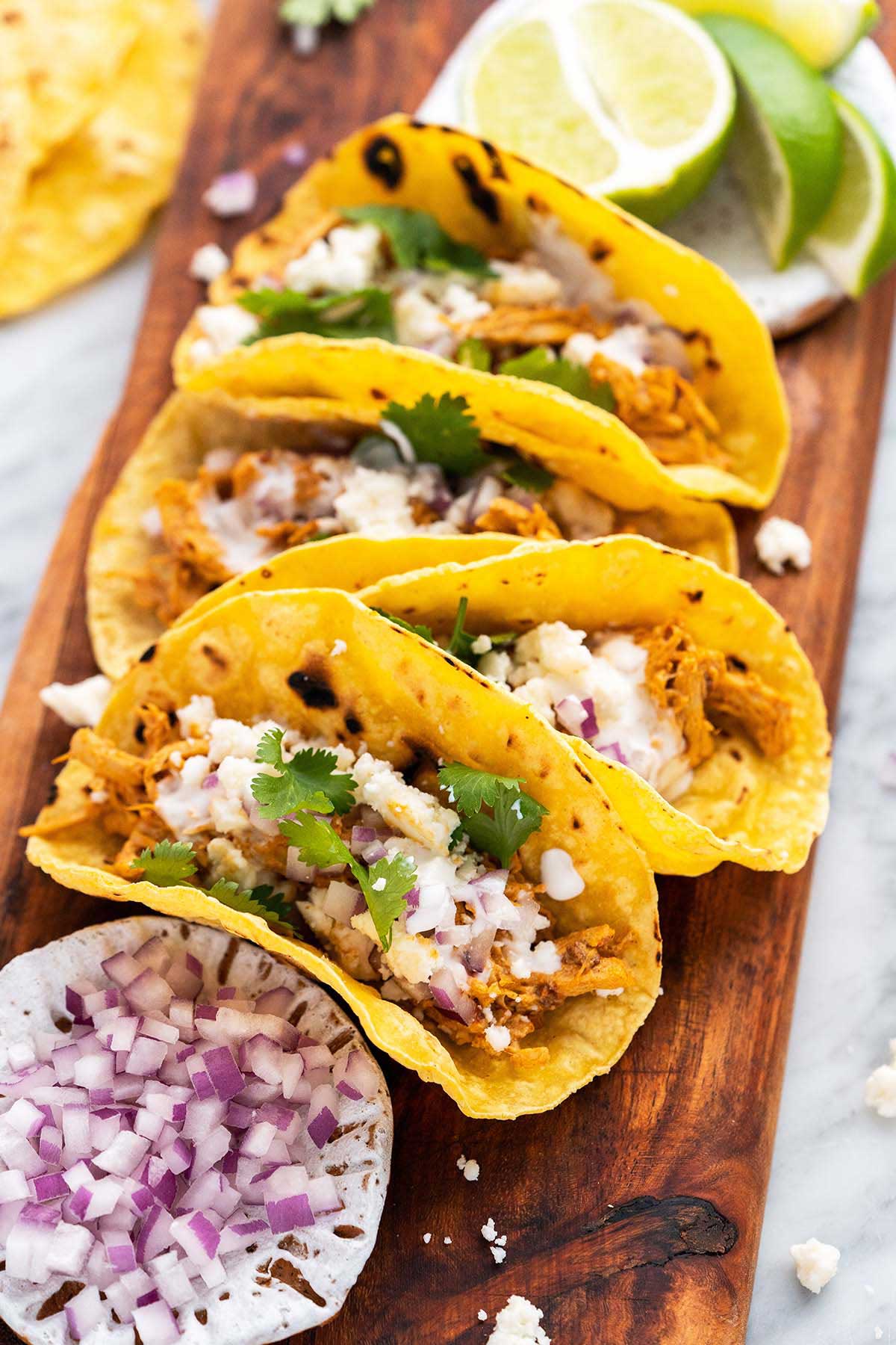 creamy chipotle shredded tacos prepared on cutting board with lime and chopped red onion in background.