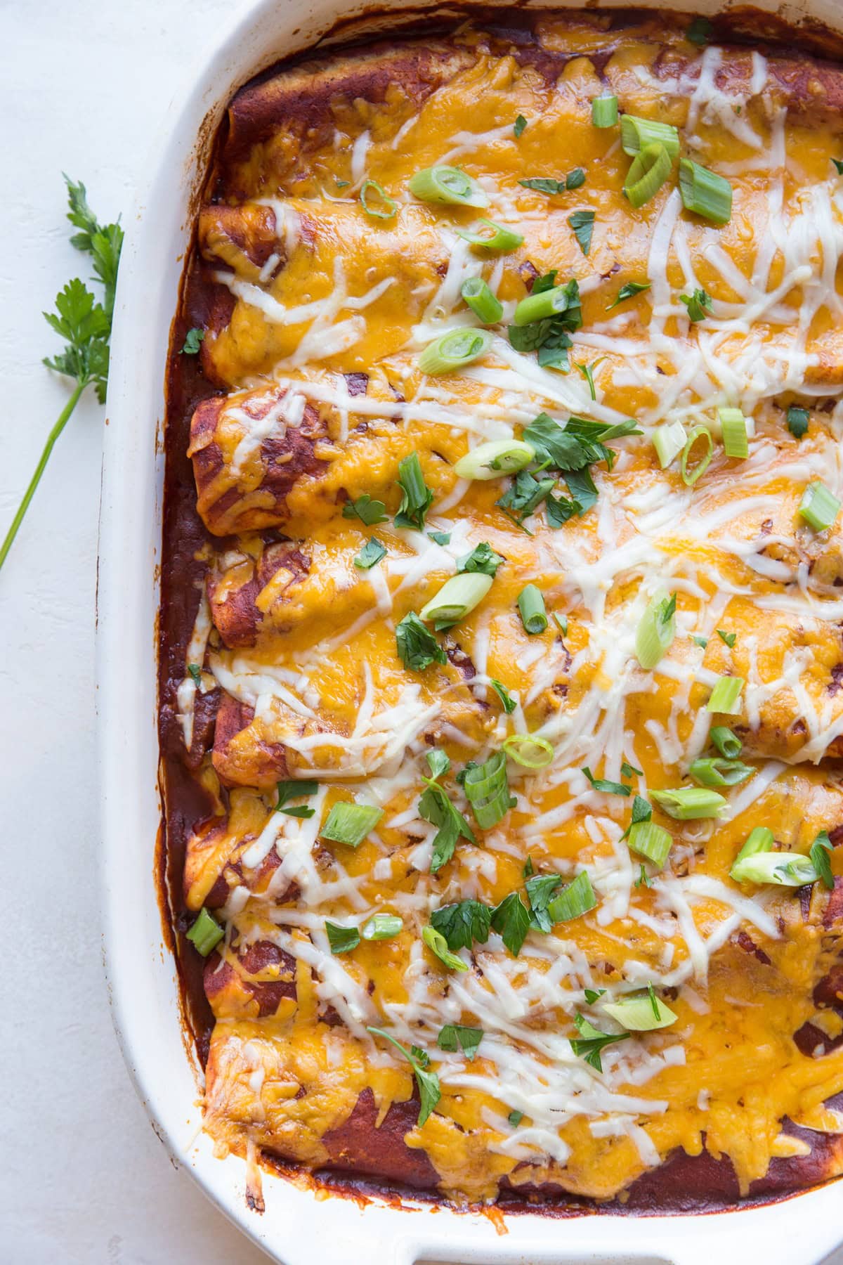 pulled pork enchiladas in white casserole dish topped with cheese and scallions.