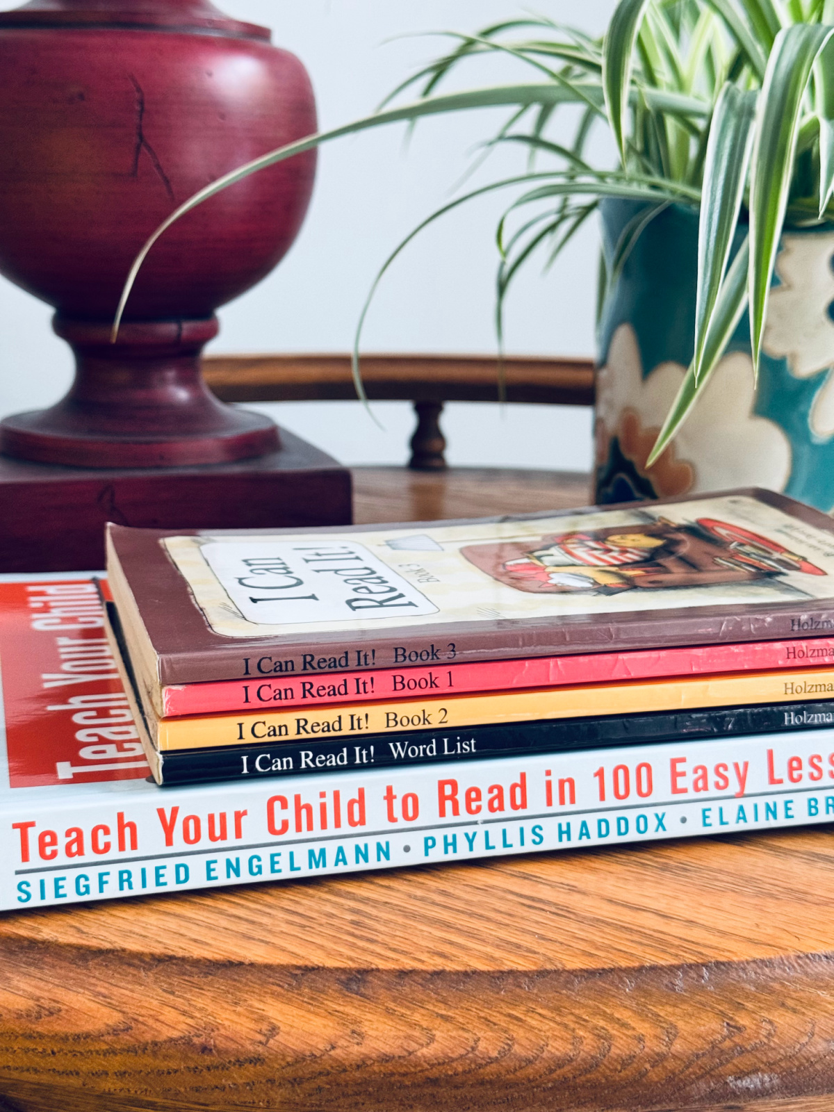 teaching reading books in a stack on a table with red lamp and plant in background.