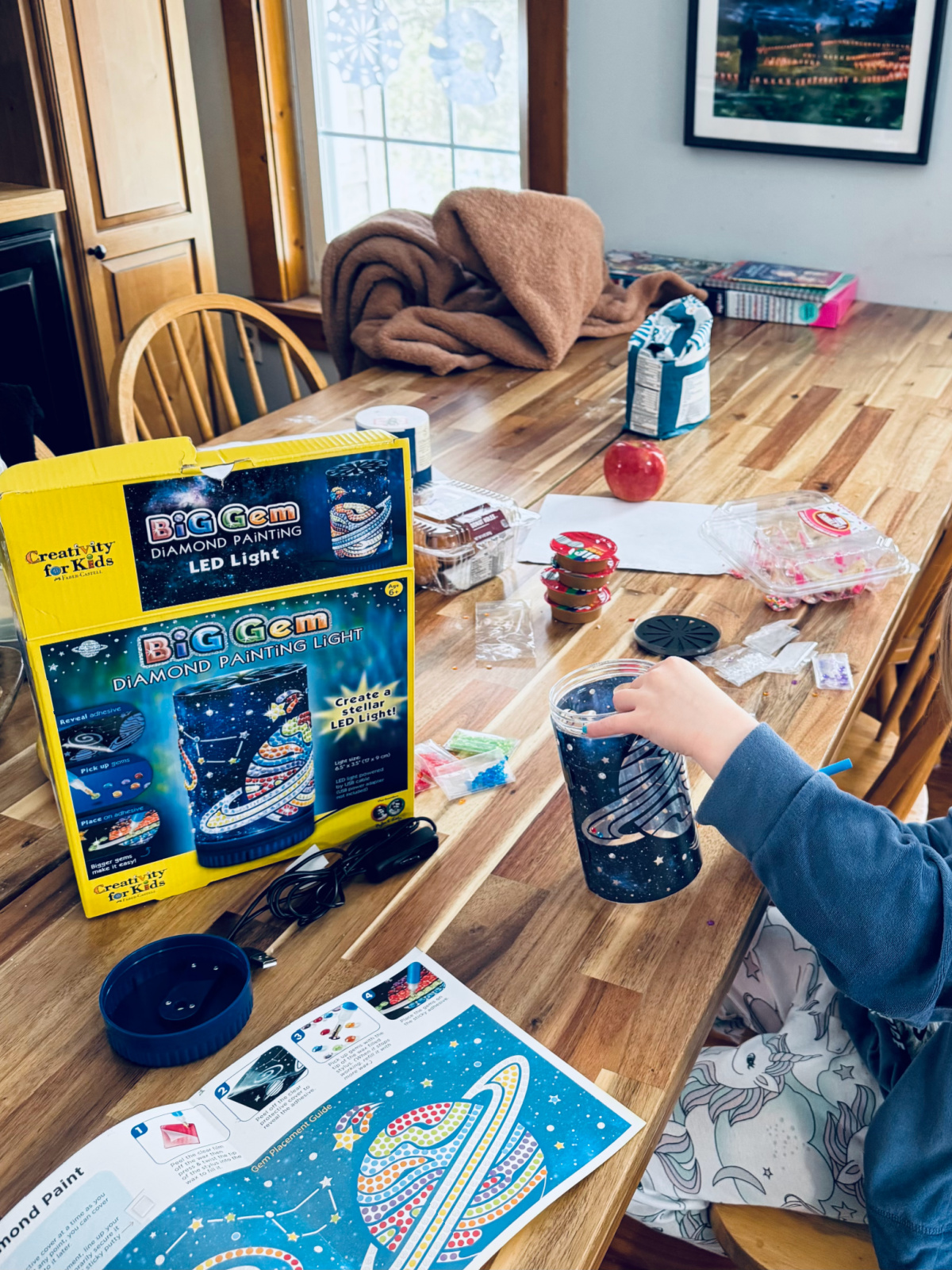 child working on a Big Gem diamond painting light kit at kitchen table.